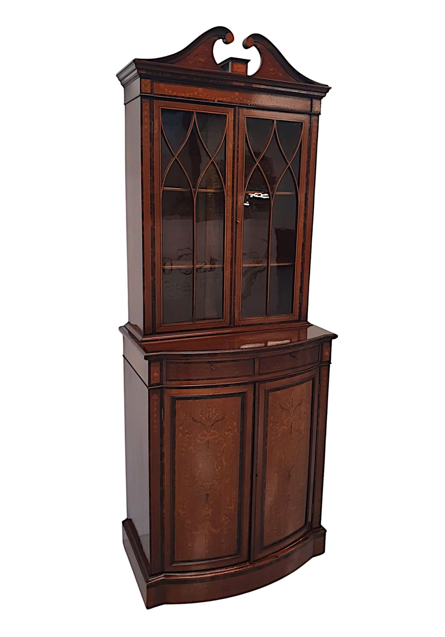 A fine Edwardian mahogany two door bookcase of neat proportions, with ebonised detail and intricate marquetry inlay throughout depicting Neoclassical motifs featuring an urn, lyres, trailing bell husks, ribbon bow swags, garlands, flowerheads and