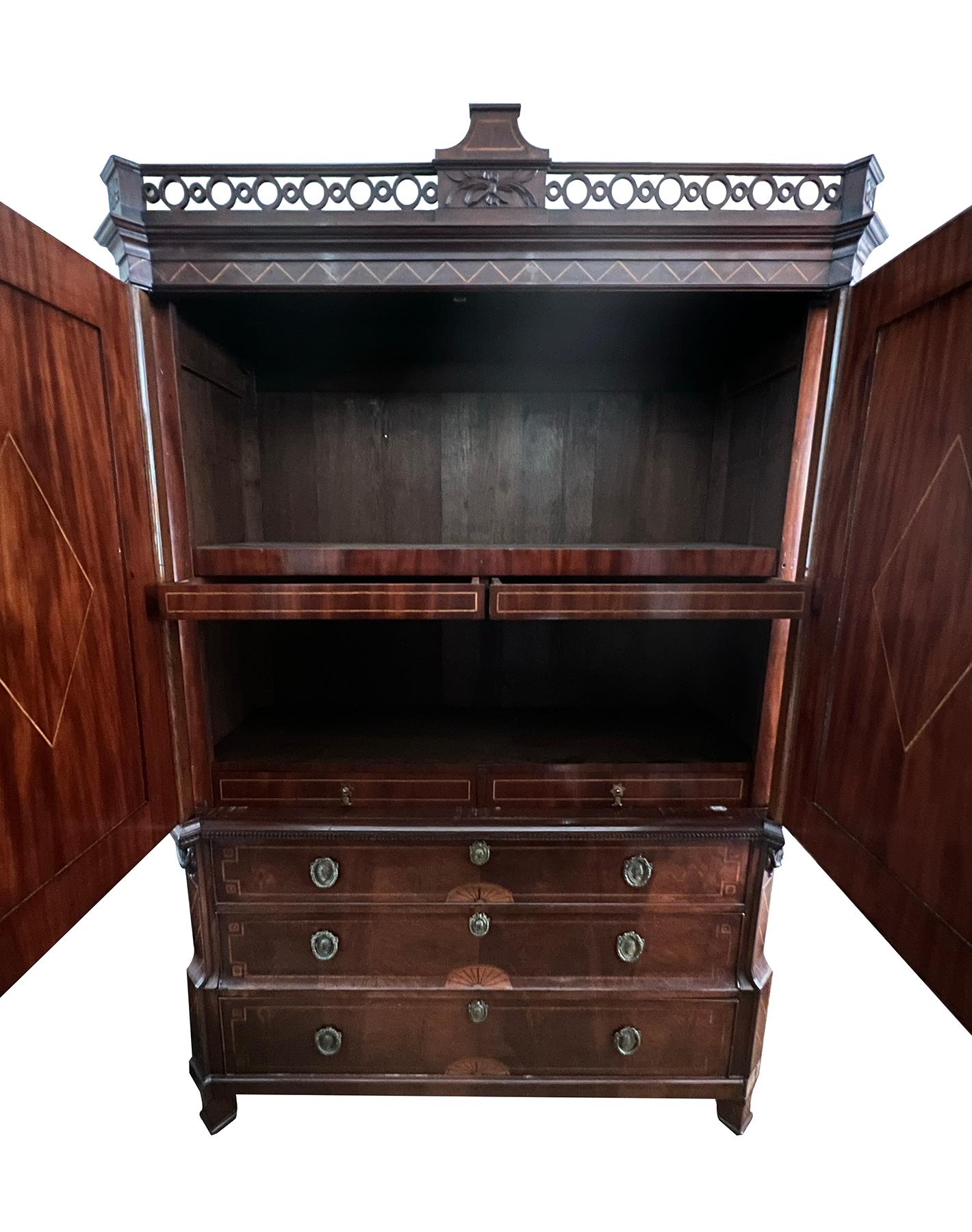 Of fine quality, the tall and impressive cabinet in the neoclassical taste with canted corners all capped by a pierced gallery above a case fitted with two hinged doors of book-matched mahogany veneer centering inlaid shell medallions below drapery