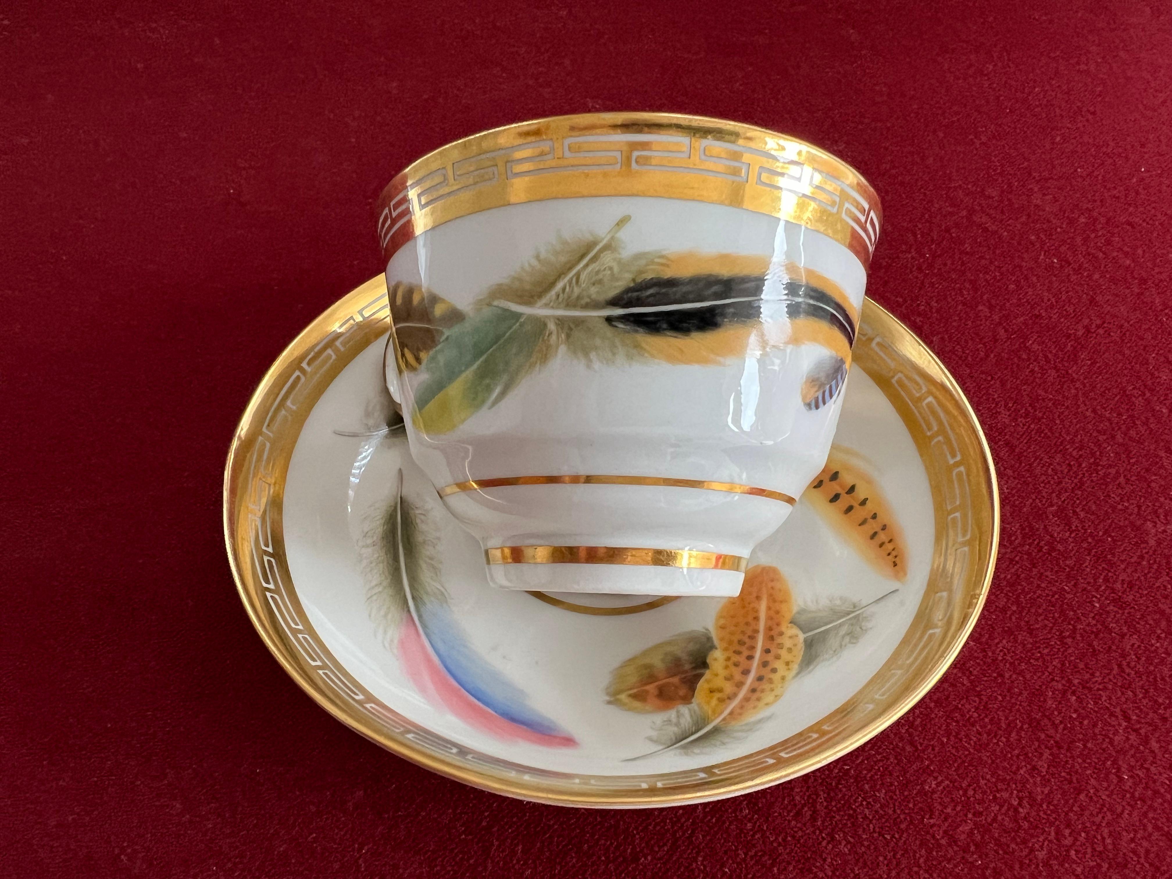 A fine Flight and Barr Worcester feather-painted teacup and saucer, circa 1800. Finely painted with a selection of colourful feathers scattered on the white ground by William Doe, within gold keyfret borders, the ring handle also edged in gold.