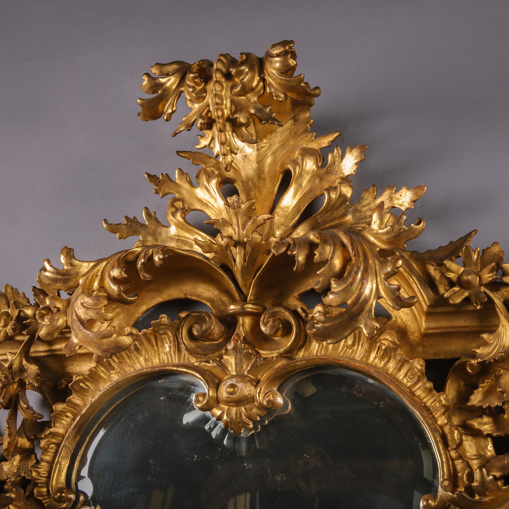 Miroir en bois doré sculpté de Florentine. 

Cet impressionnant miroir en bois doré sculpté présente une plaque biseautée en forme de cartouche, à l'intérieur d'un cadre à acanthes sculptées en rocaille et percées, avec des roses de rocaille, des
