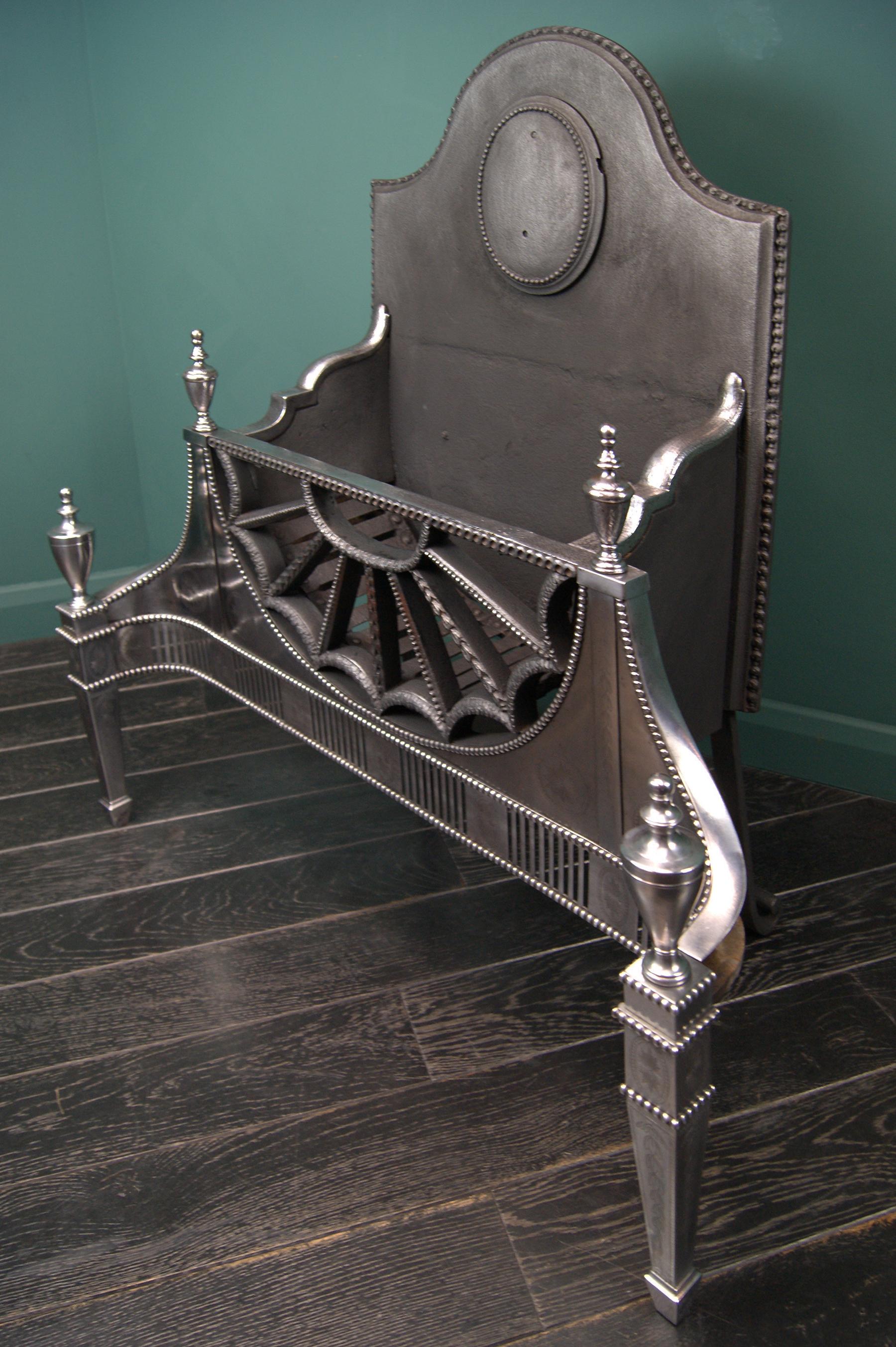 A fine free-standing fire grate in the manner of Robert Adam with a semi-circular fan-fronted fire basket adorned with harebells and interlocking circles. The cut-steel polished front and fret are intricately engraved. The pierced fluted fret is set