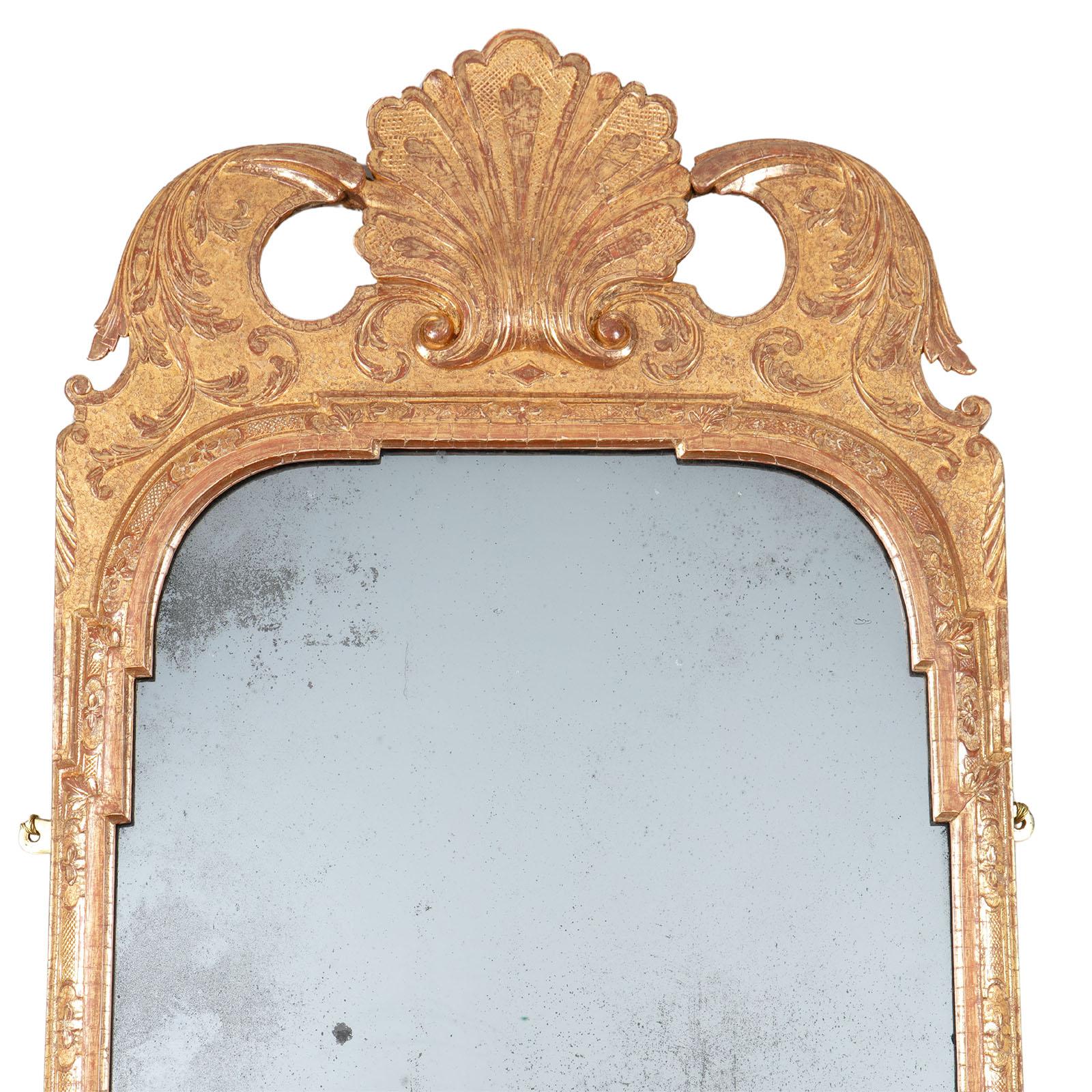 Miroir mural en gesso doré du début du XVIIIe siècle. L'encadrement est orné de coquilles au sommet et au tablier, de sangles brunies en relief et de vignes en volutes sur un fond estampé contrasté. Conservant sa plaque de rétroviseur d'origine. La
