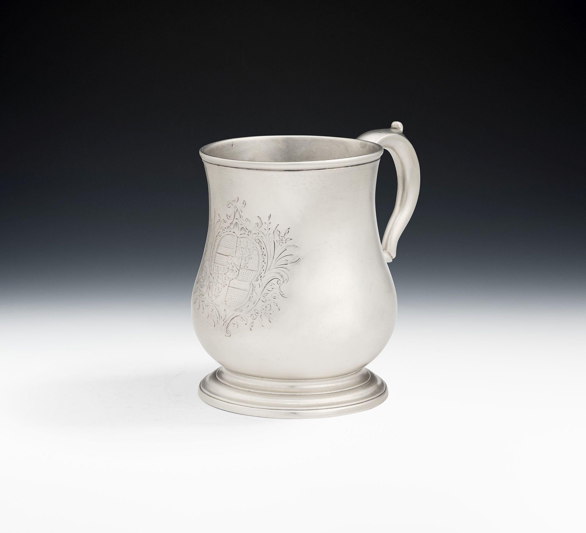This fine mug stands on an applied circular foot and has a baluster main body and everted rim. This piece has a scroll handle and the front is engraved with a contemporary Armorial surrounded by a floral and foliate spray cartouche. The mug is fully