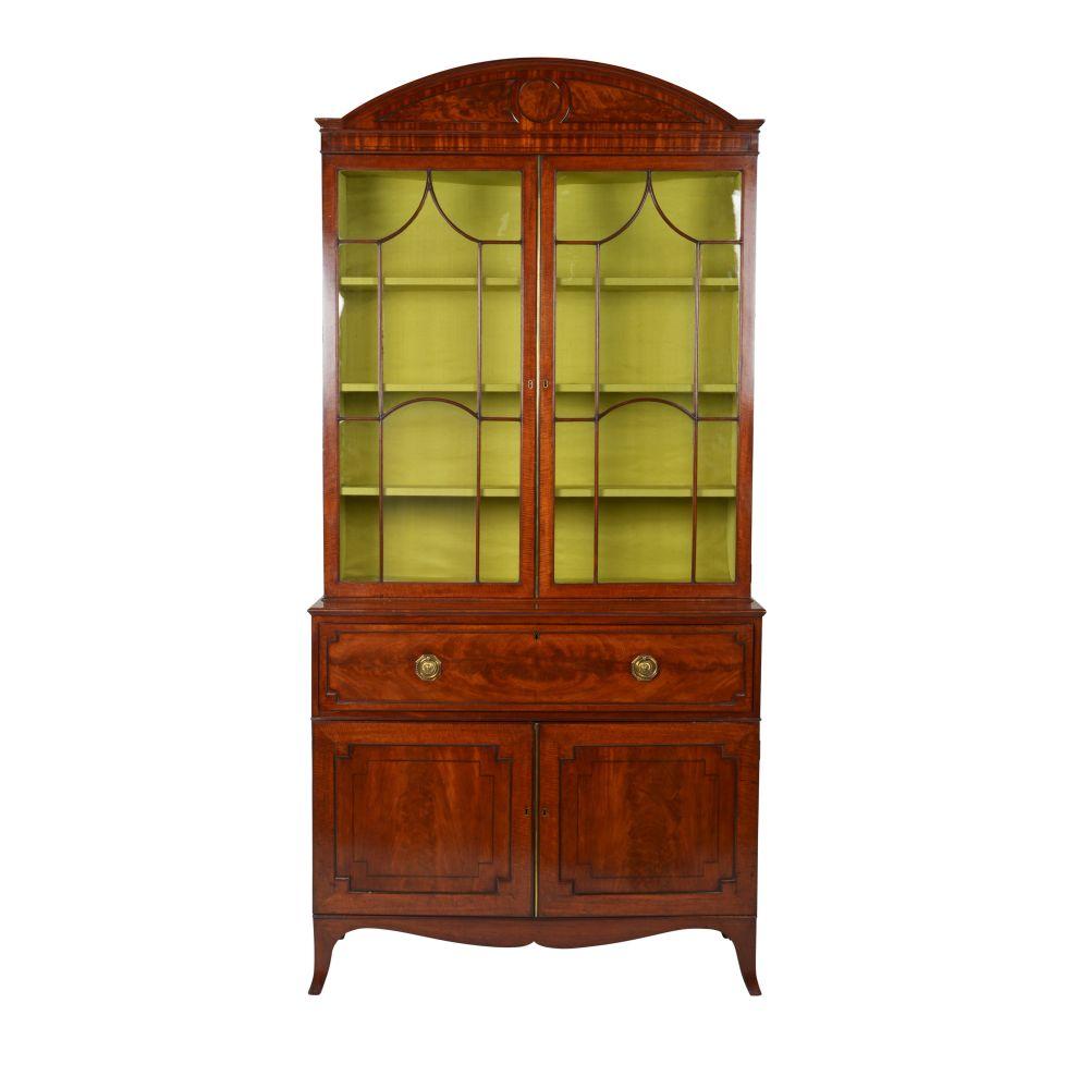 The arched pediment centered by paneled roundel, over two glazed doors with pointed astragals opening to a chartreuse silk-lined interior with shelves; the lower part with a pullout leather-lined writing surface and fitted interior comprising small