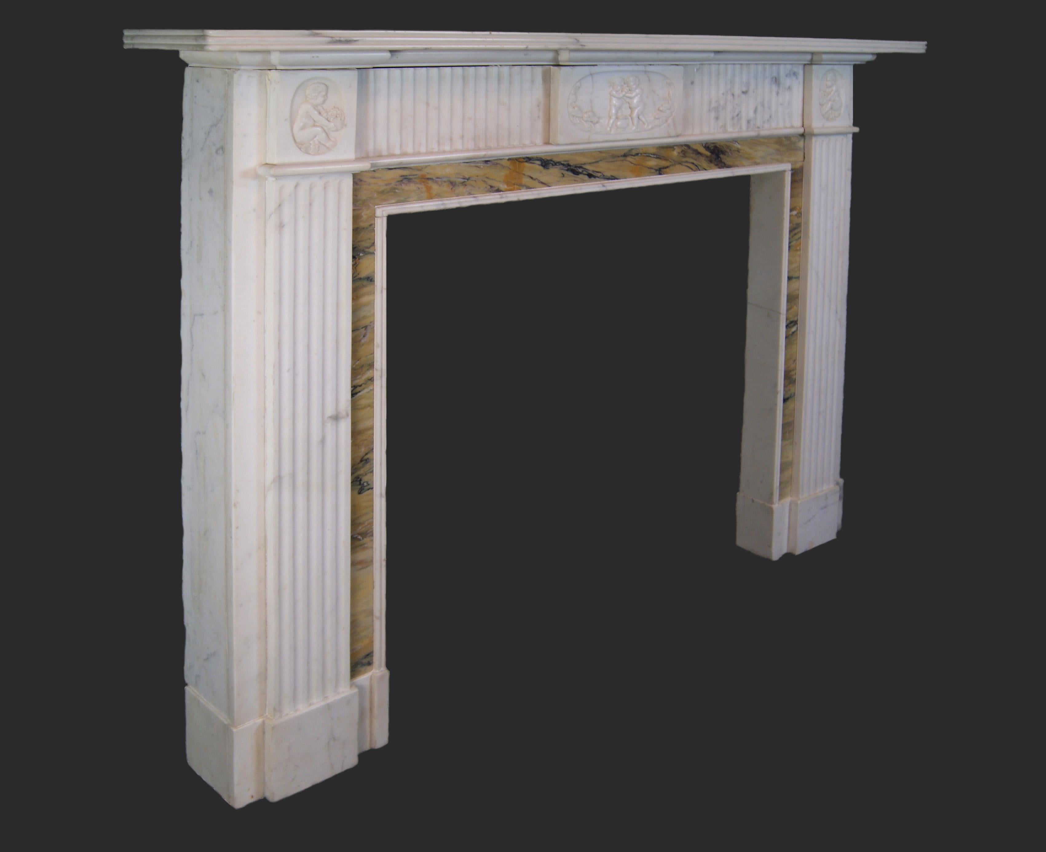 Belle cheminée néo-classique anglaise de style néo-géorgien, sculptée dans un marbre blanc légèrement veiné, avec incrustation de Sienne.  La tablette centrale et les blocs d'angle sont sculptés en relief et représentent des putti, interrompus par
