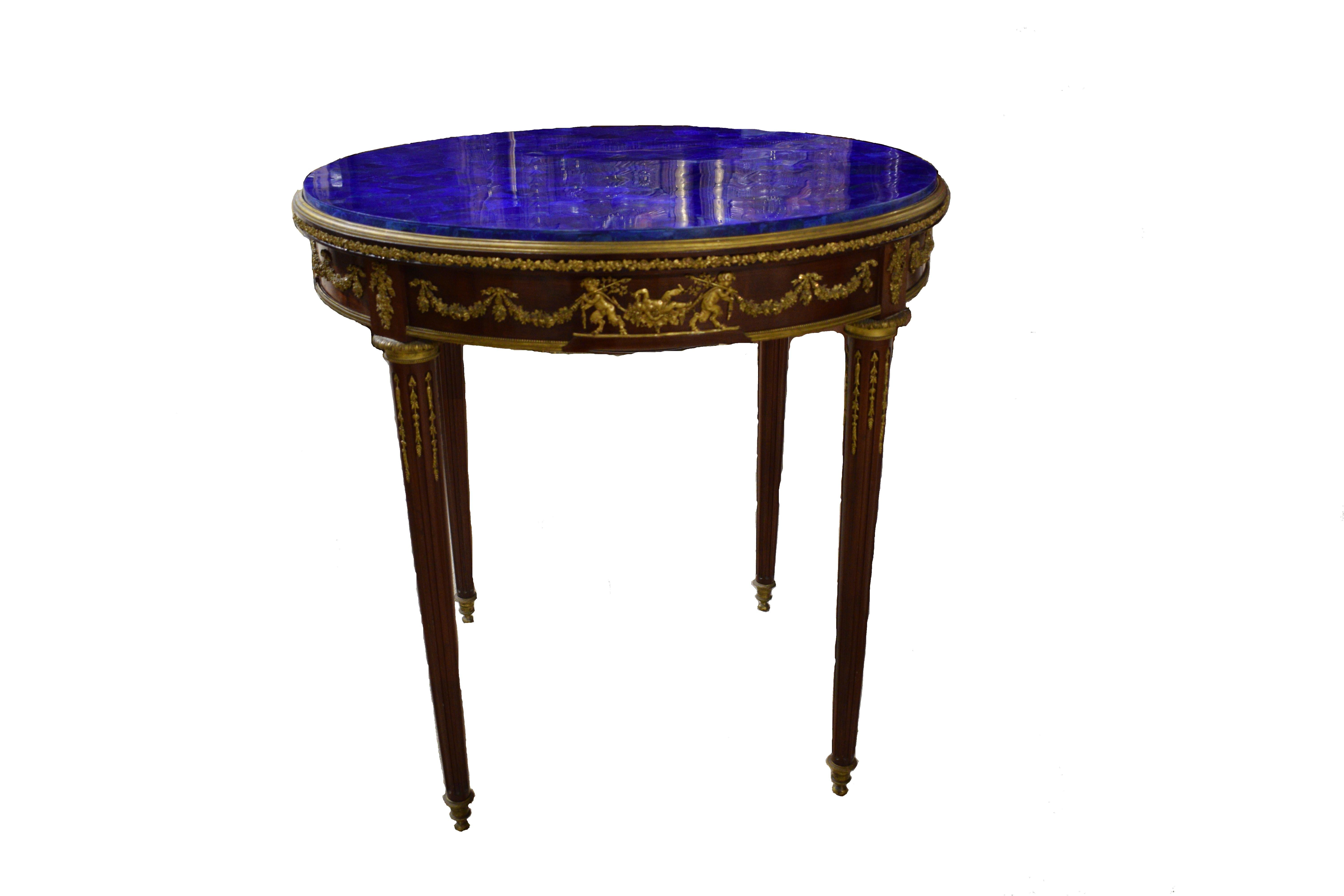 A fine mahogany gilt bronze mounted center table featuring a Lapis Lazuli Top. The bronze mounts, of extraordinary quality, depict frolicking children and baby satire's carrying decorative garlands. Raised on four bronze mounted reeded