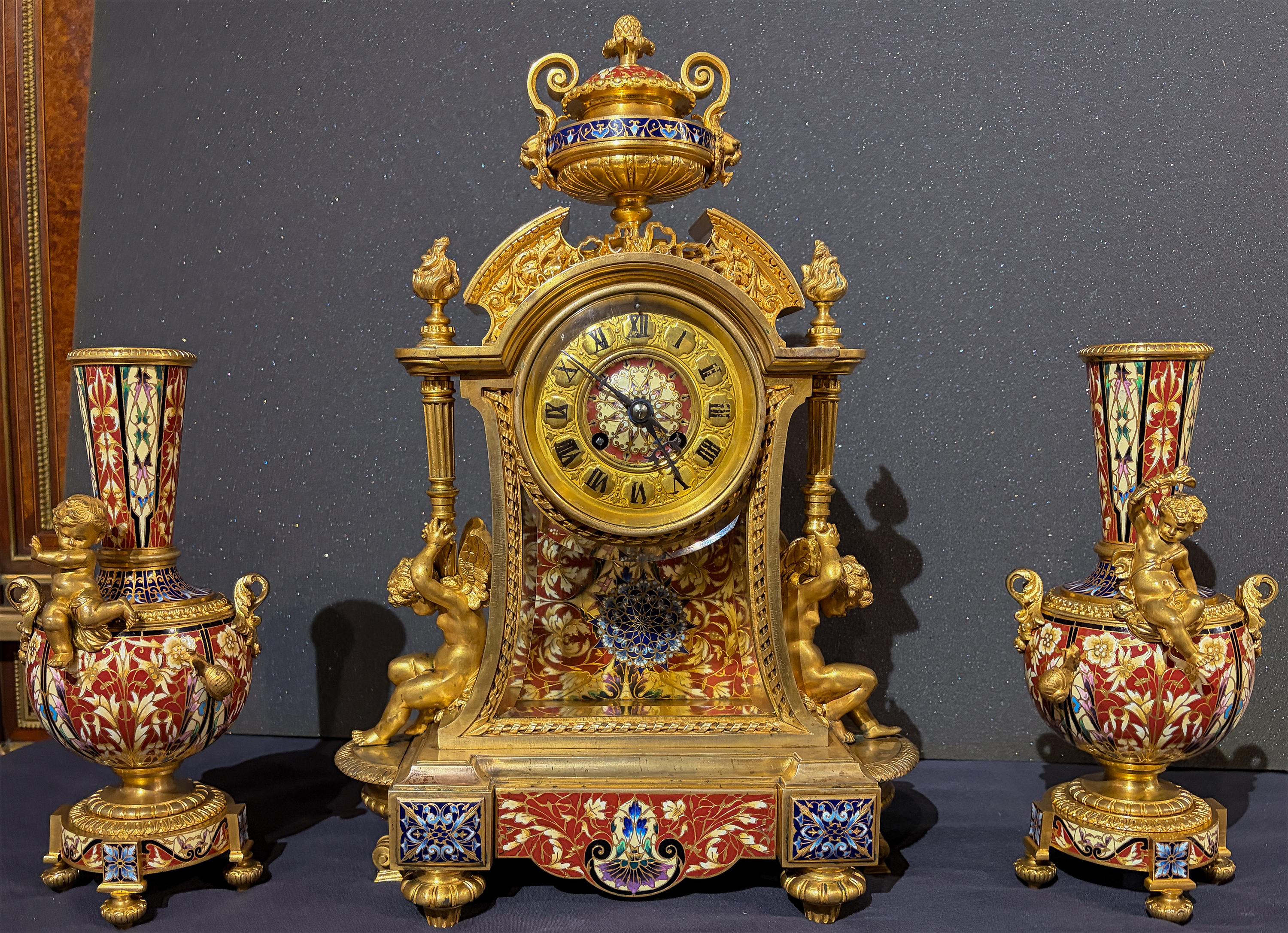 Un raffinato set di orologi francesi Japy Frères in bronzo dorato e smalto rosso con vasi di putti e lumache 

Il set comprende un orologio architettonico champlevé con corpo in vetro smussato e pendolo a stella champlevé blu, affiancato da una