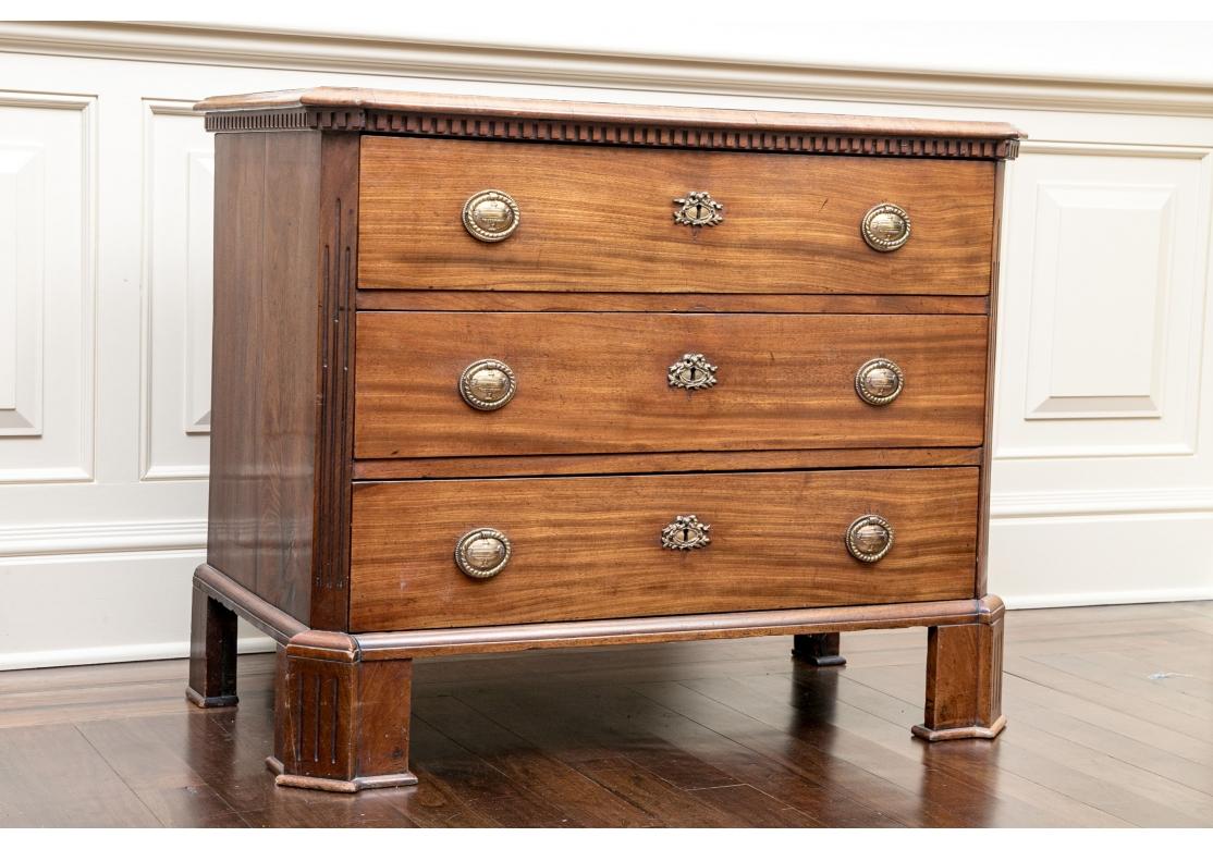 An elegant and very well made Antique three drawer chest with Canted corners, handsome chosen wood, Urn Motif Brass Ring Pulls, Ribbon Motif Escutcheons, inlaid Diamond shaped center top inset, Dentil  Molding surround and bold pronounced Canted and
