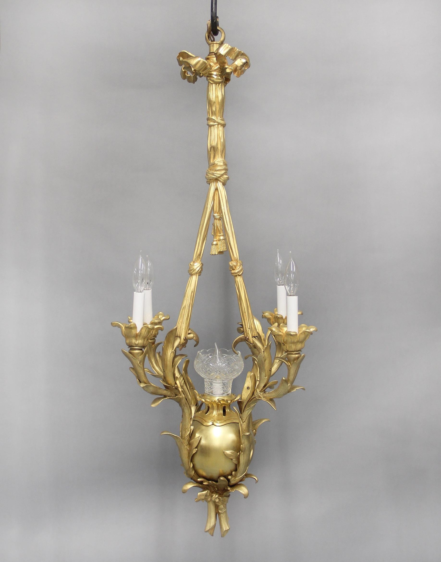 A Fine Late 19th Century Gilt Bronze Five Light Chandelier

The bow tied crown with a flowing curtain body leading to crossed tassels, splitting down and attaching to four foliate designed arms, the ball shaped base with an etched shade and single