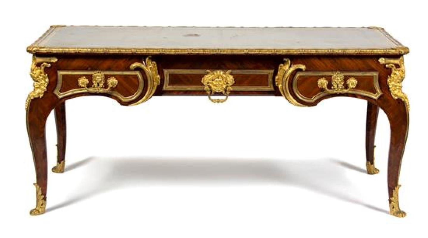 A fine Louis XV style gilt bronze-mounted tulipwood bureau plat.
Late 19th century. The replaced gilt-stamped green leather writing surface within gilt bronze lappet and egg-and-dart borders over three frieze drawers with masques, the reverse with