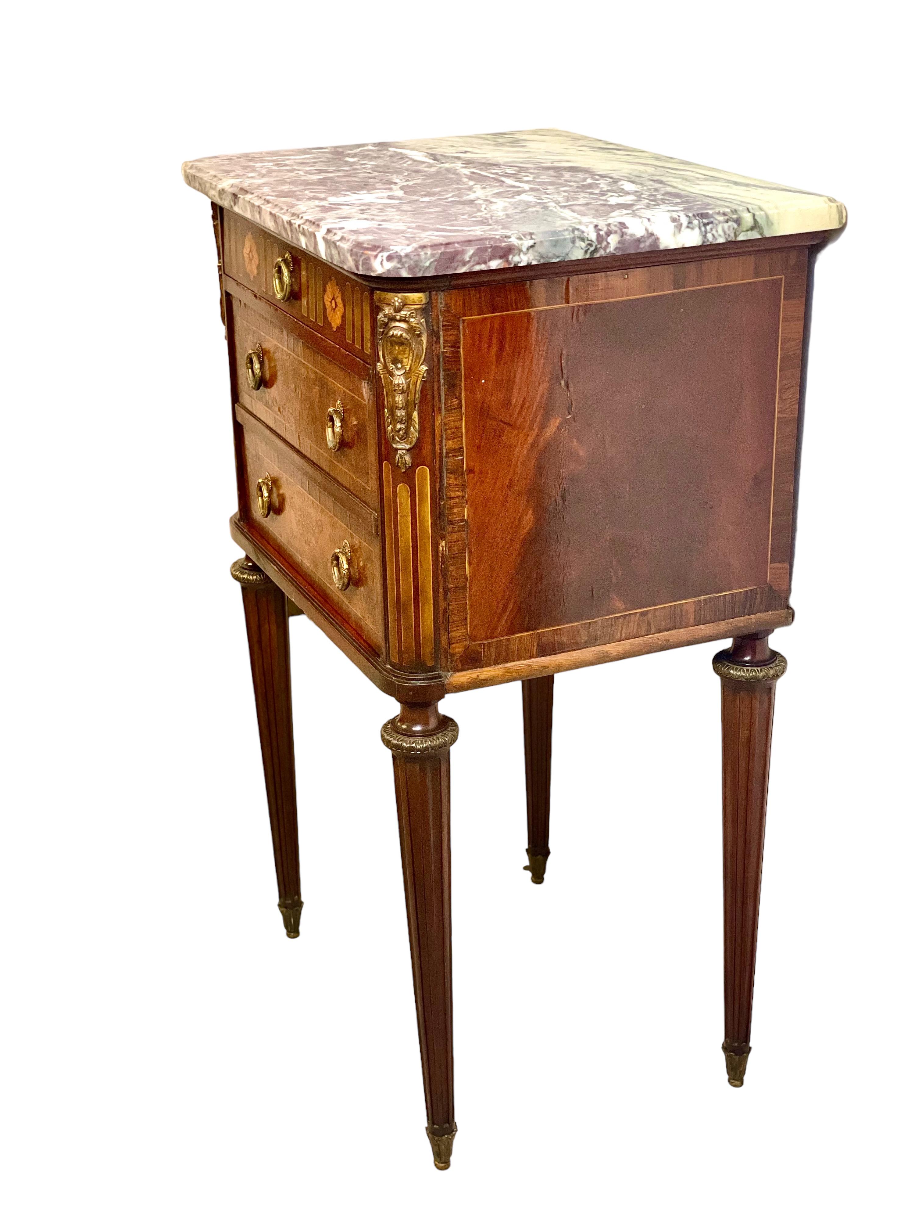 A fine Louis XVI style bedside table by renowned Parisian cabinet maker Soubrier, in burr wood veneer with an inlaid decoration of flowers and simulated grooves. This impressive cabinet is topped with a stunning grey and white marbled granite top