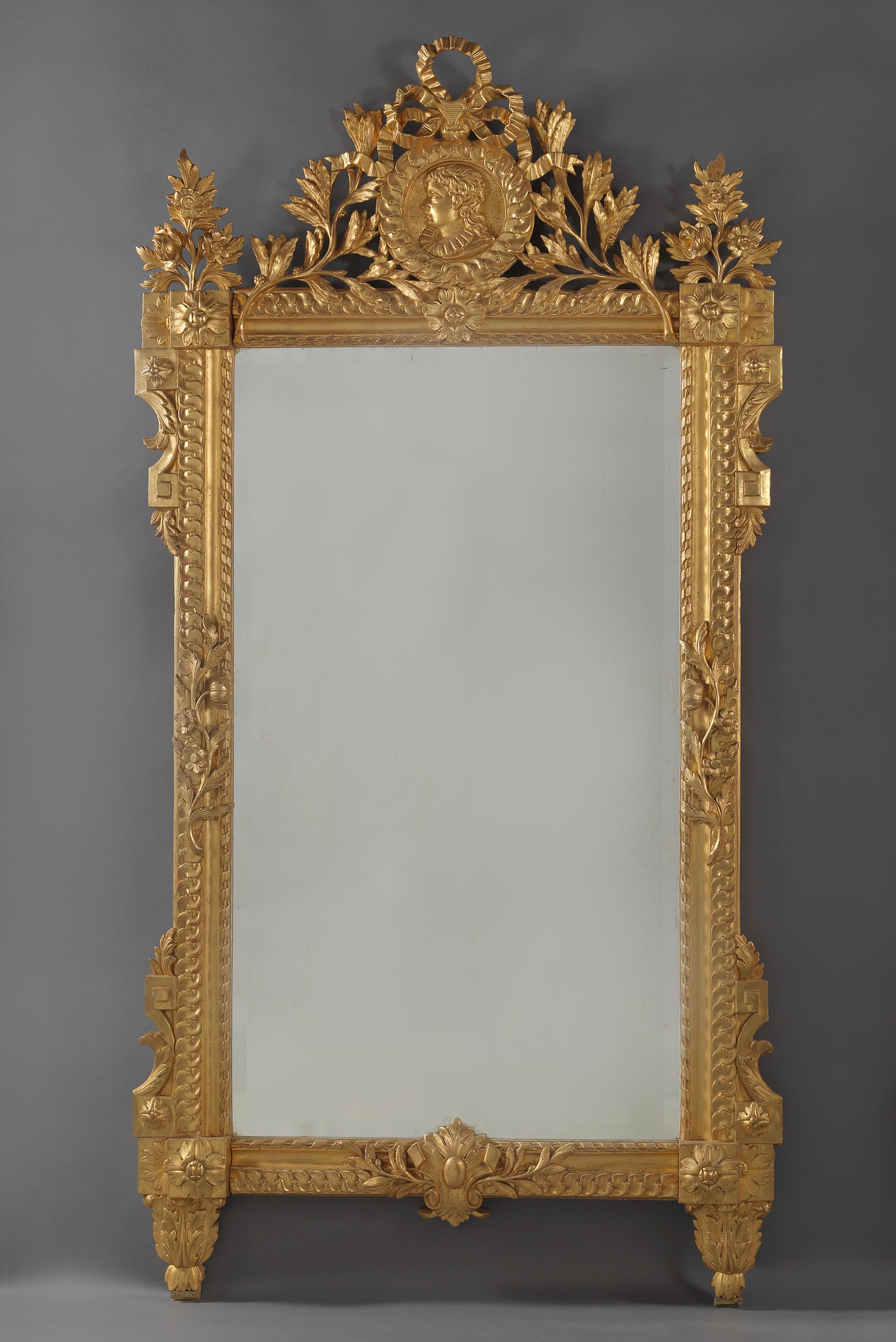 A fine Louis XVI style carved giltwood mirror, the cresting carved with a portrait roundel of a young man in profile. 

This impressive mirror is richly carved with a ribbon tied laurel cresting centred by a guilloche framed roundel, carved with a