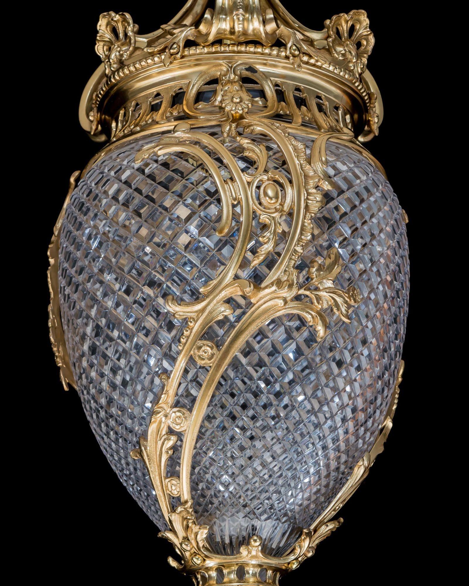 The gilt lacquered metalwork of elaborate asymmetrical design mounting a flat diamond cut glass urn.