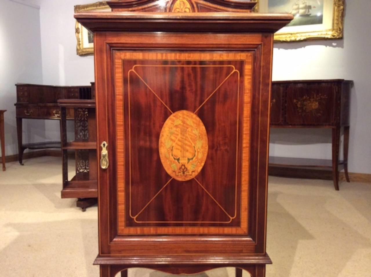 A fine mahogany and satinwood marquetry inlaid Edwardian period music cabinet by Shapland & Petter. The back with a shaped gallery and a satinwood and marquetry inlaid panel depicting the arts, above a central rectangular flamed mahogany door with