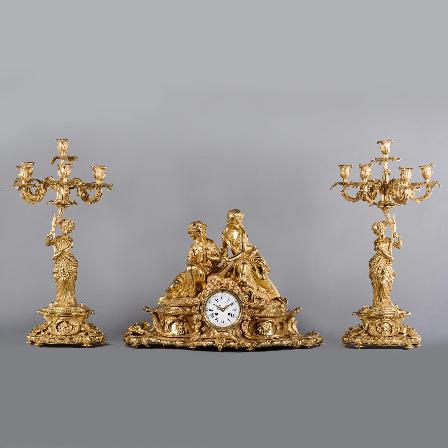  A Fine Napoléon III Gilt-Bronze Three Piece Clock Garniture

Comprising a mantel clock and a pair of seven-light figural candelabra. Designed as a celebration of music and lyric poetry with Grecian classical nymphs. The mantle clock modelled with