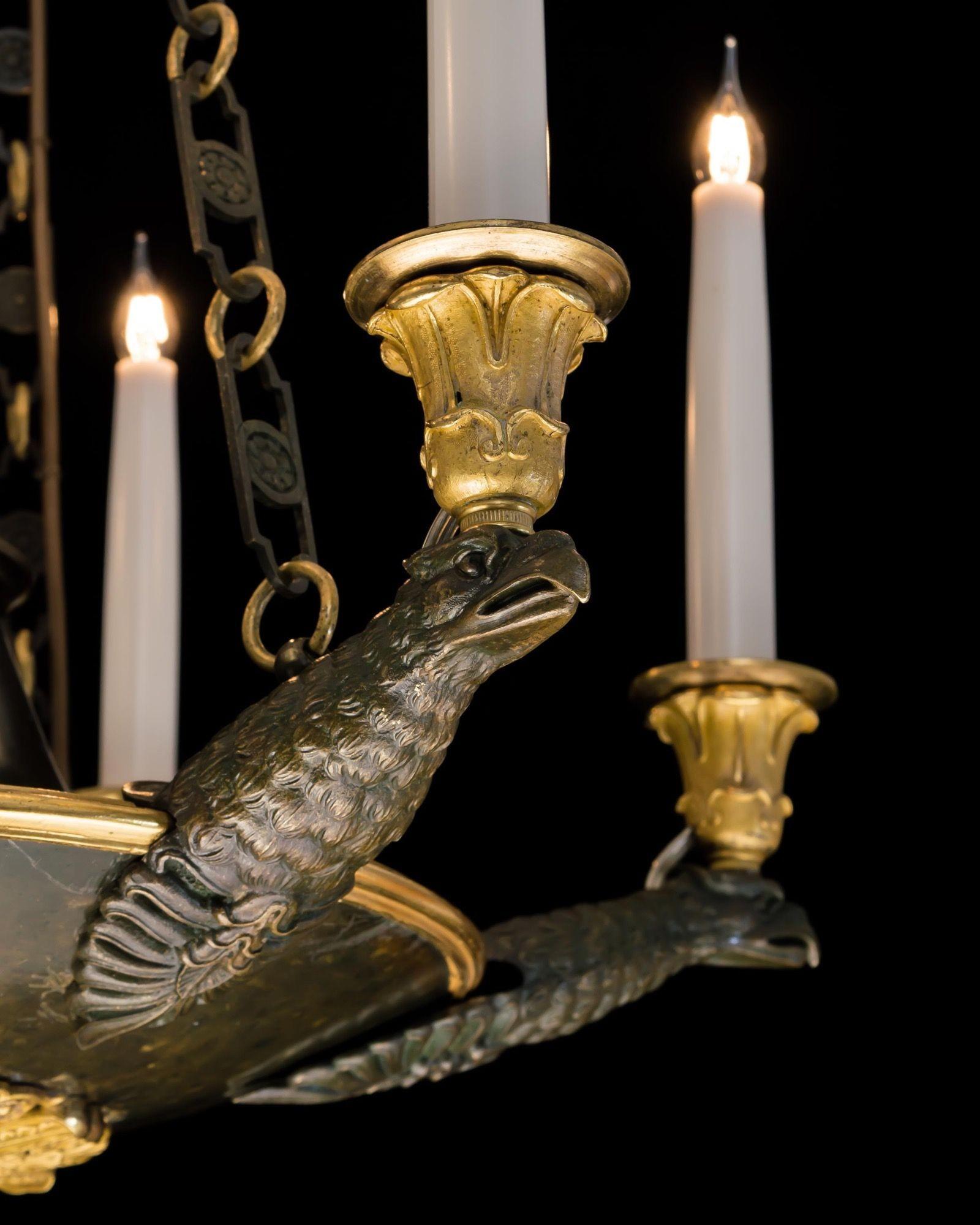 La cornice brevettata in bronzo, montata con ormolatura finemente cesellata, emette sei teste d'aquila che sostengono i beccucci delle candele e i salvadanai, sospesi su tre catene da una corona foliata.