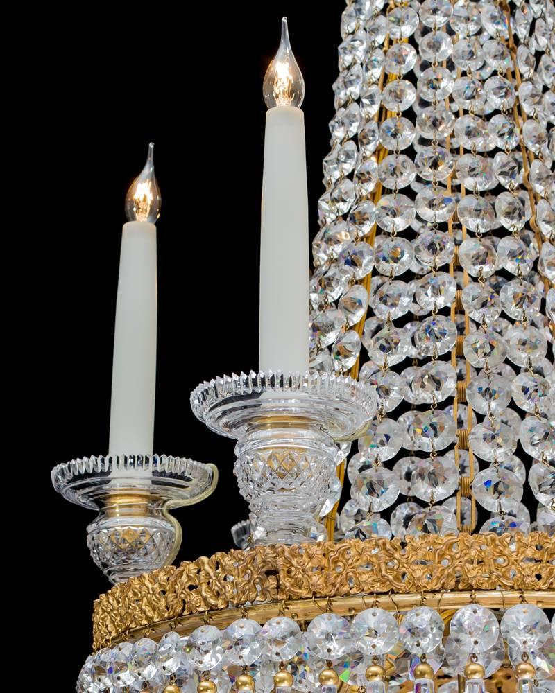 A fine Regency chandelier of tent and basket design with double ormolu bands the larger main ring issuing six diamond cut-glass candle nozzles, the chandelier is hung with double cut spangles and ormolu caped icicle drops terminating with lapidary