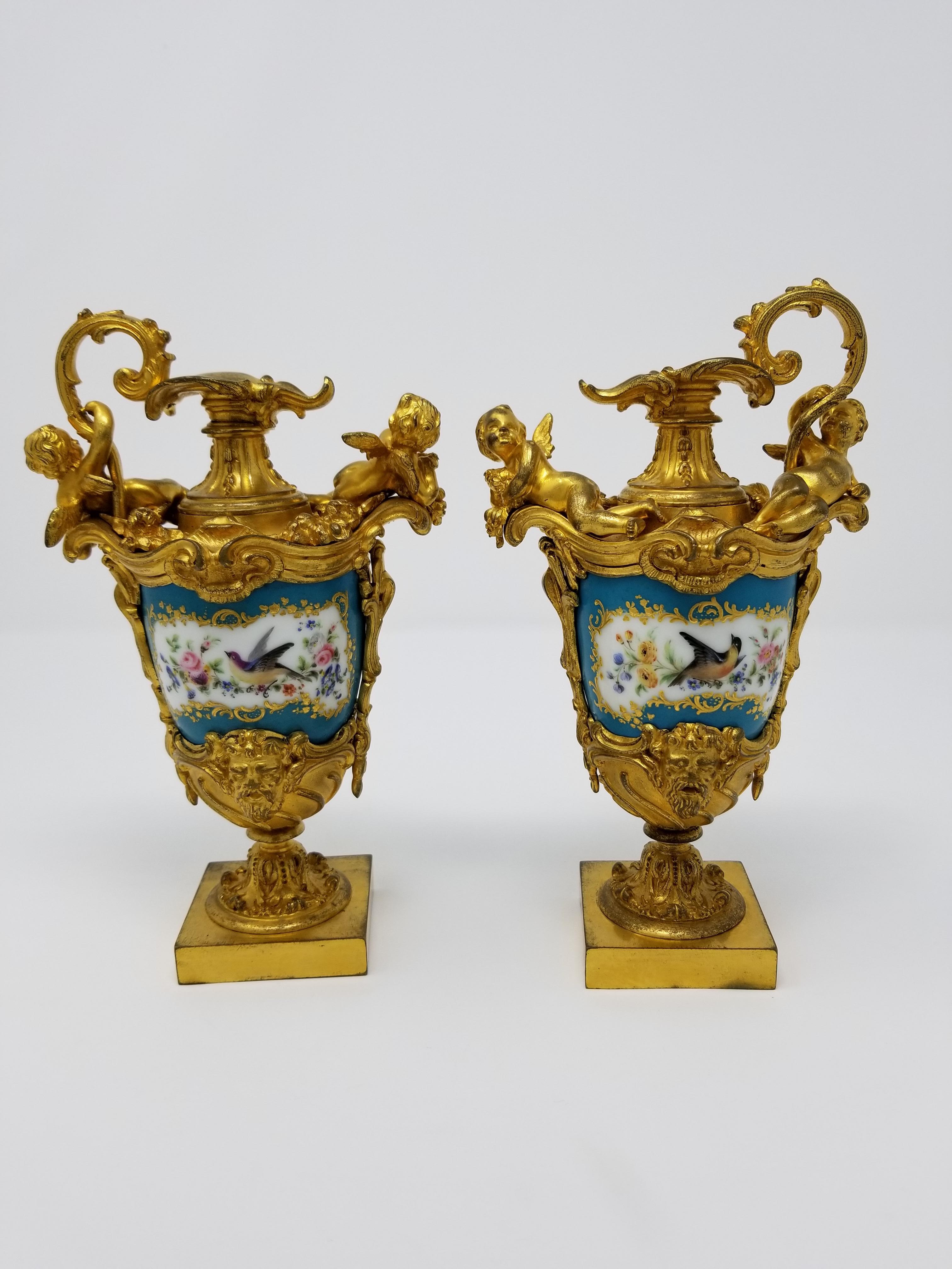 A beautiful pair of 19th century French Sèvres style Porcelain and ormolu-mounted ewers which are hand painted in Sèvres celest blue color porcelain. Each ewer is very finely hand painted with bird scenes in poly-chrome enamels on one side; and