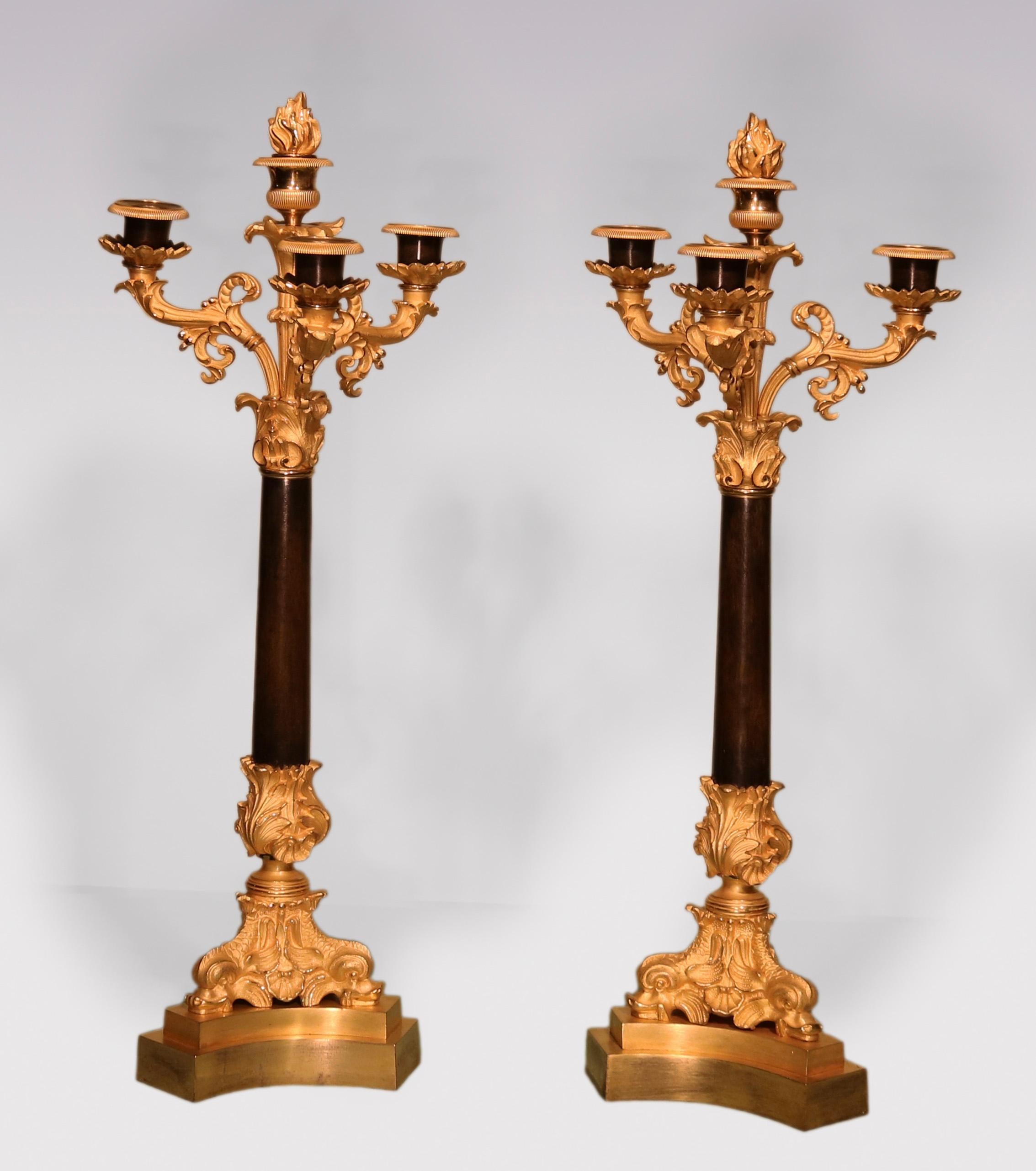 An attractive pair of early 19th Century Bronze and Ormolu 4 light Candelabra with removeable flame finial to centre light, supported on scrolled arms above tapering stems raised on triple Dolphins, ending on triform bases.