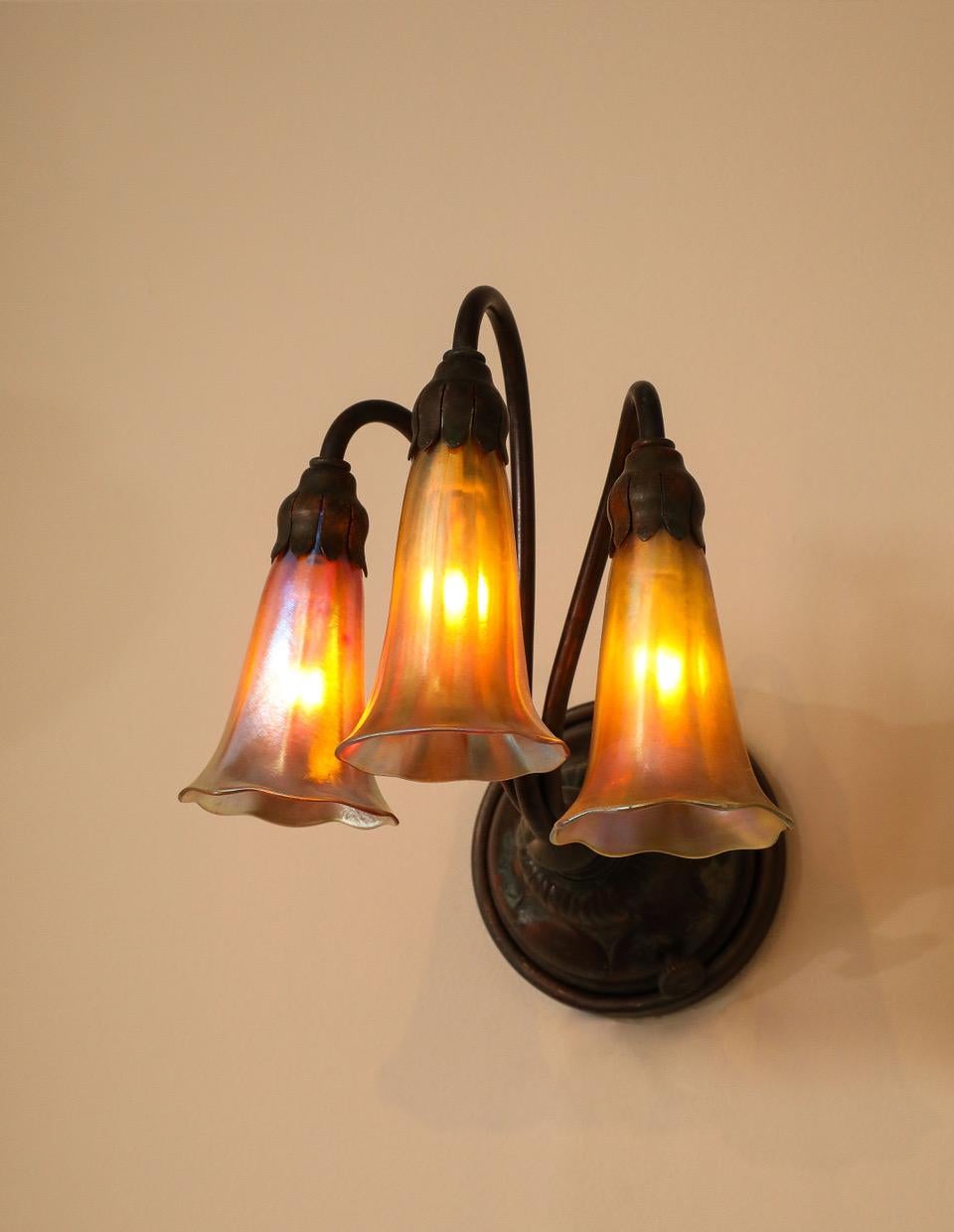 Each bronze wall fixture with three arms each supporting an art glass Lily, signed L.C.T. 

Electric is UL Certified.

Provenance: Originally purchased from Macklowe Gallery by present owner.