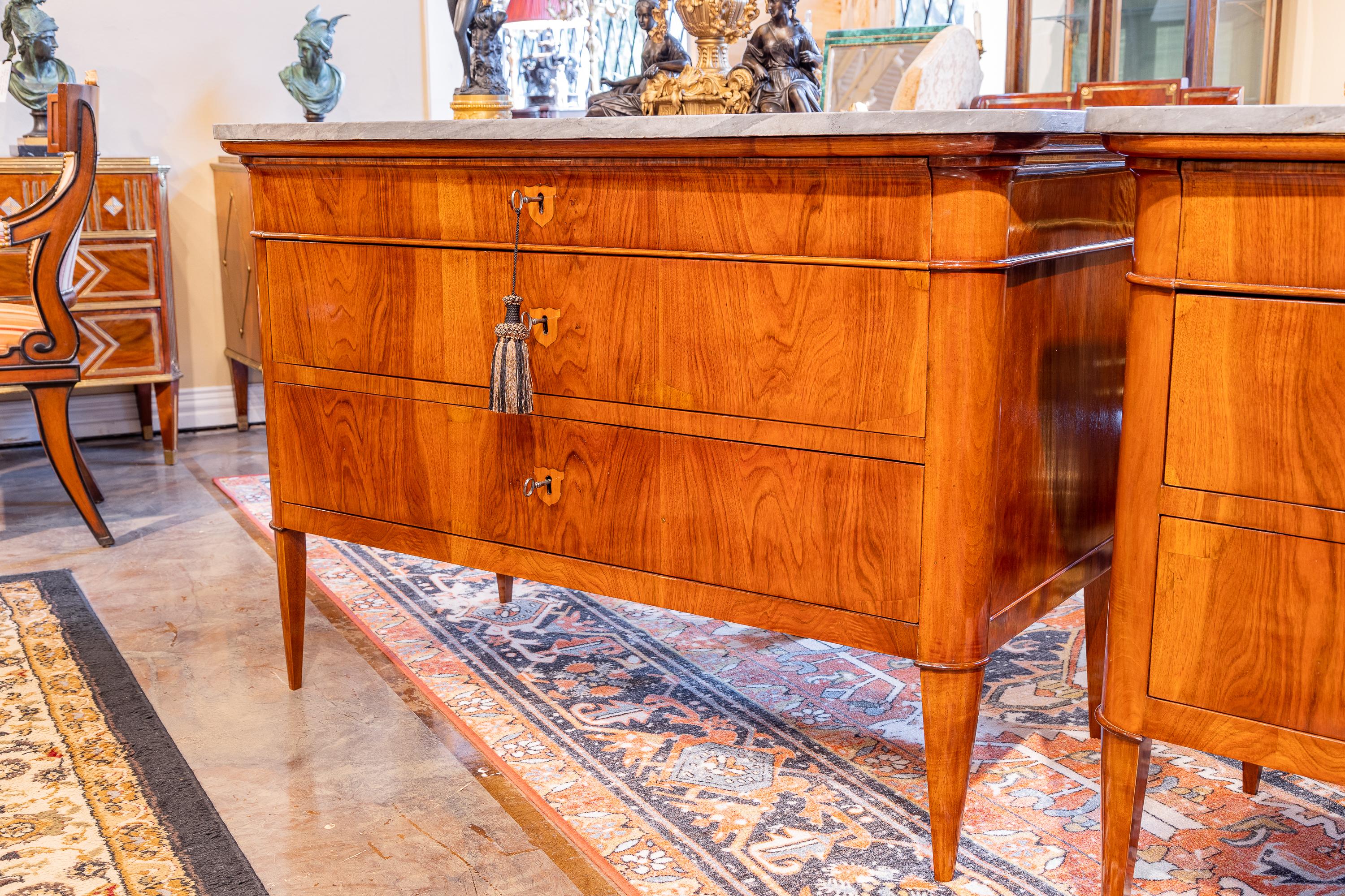 A fine pair of Biedermeier period marble top commodes. Fine walnut with satinwood inlay and original grey marble tops.