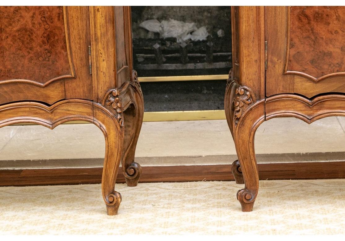 A particularly elegant and well made cabinet pair with handsome chosen veneers and a very interesting form. The serpentine shaped cases with figured wood tops, shaped side and door panels, and carved moldings overall. One shelf inside. Carved floral