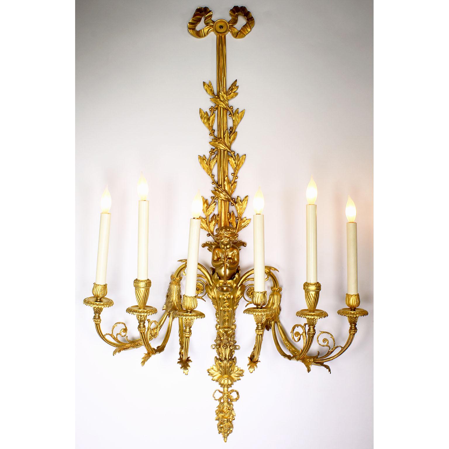 A very fine pair of French Belle Époque Louis XV Style 19th/20th century six light gilt-bronze figural wall sconces, each modeled as a ribbon-suspended trumpeting Putto term, issuing six foliate candle-arms, the back-plates stamped 6191. All