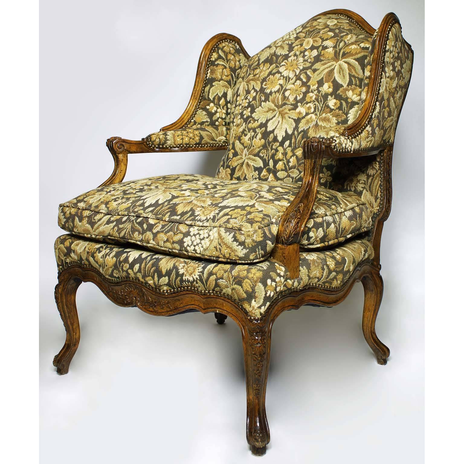 A fine pair of French Louis XV style carved walnut wingback fauteuil armchairs. The finely carved winged walnut frames upholstered in a verdure floral fabric with a cushion seat and upholstered elbow armrests, circa mid-20th century.

Measures: