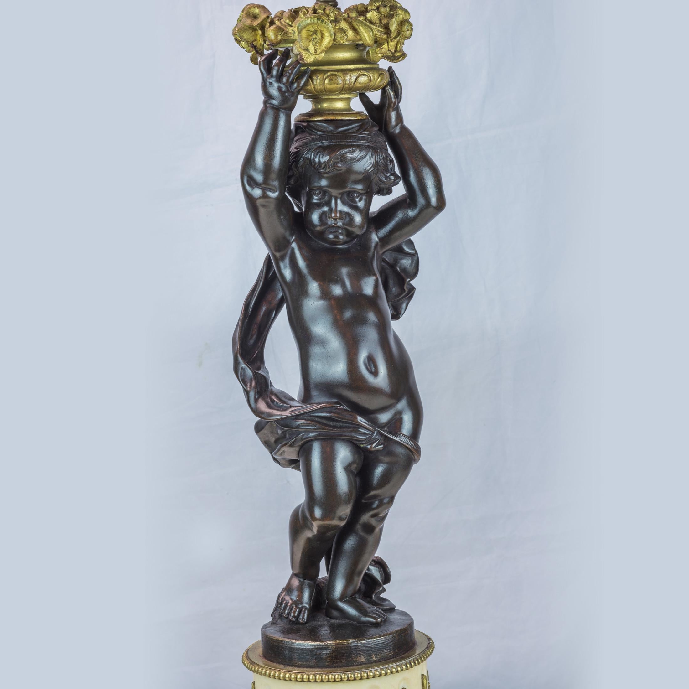 A fine pair of French patinated bronze and gilt metal figural lamps

Each cast as a putto supporting a flower filled urn, raised on a gilt metal mounted white alabaster pedestal set on toupee feet.
Date: 19th Century
Dimension: H: 31 x W: 7 1/2.