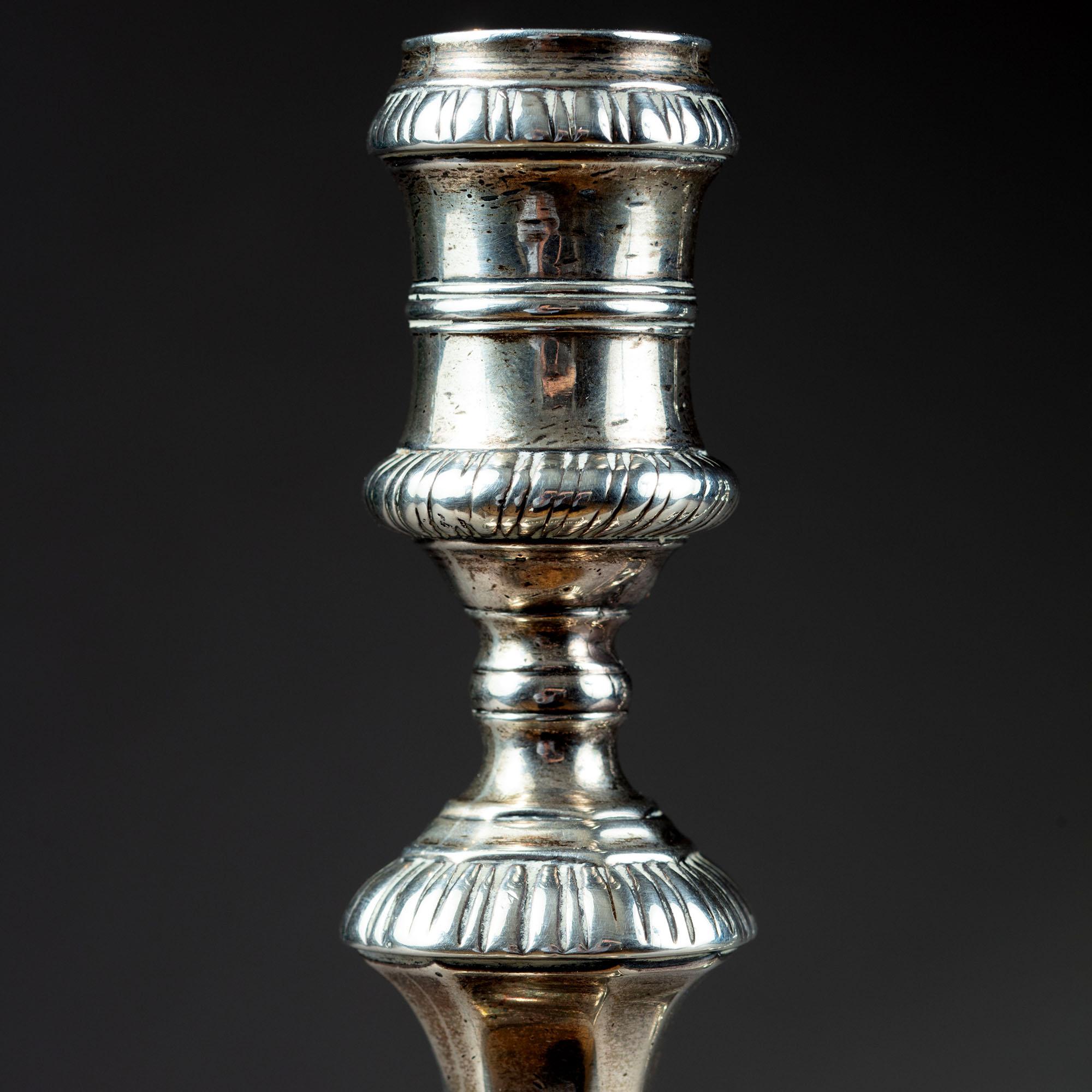 Coppia di candelabri in argento di Giorgio II con steli a più nodi sopra basi quadrate, con pozzetto quadrato bombato e bordi a gadroon.

Realizzato dall'argentiere William Cafe, Londra, 1758. John Cafe era un argentiere londinese rinomato per la