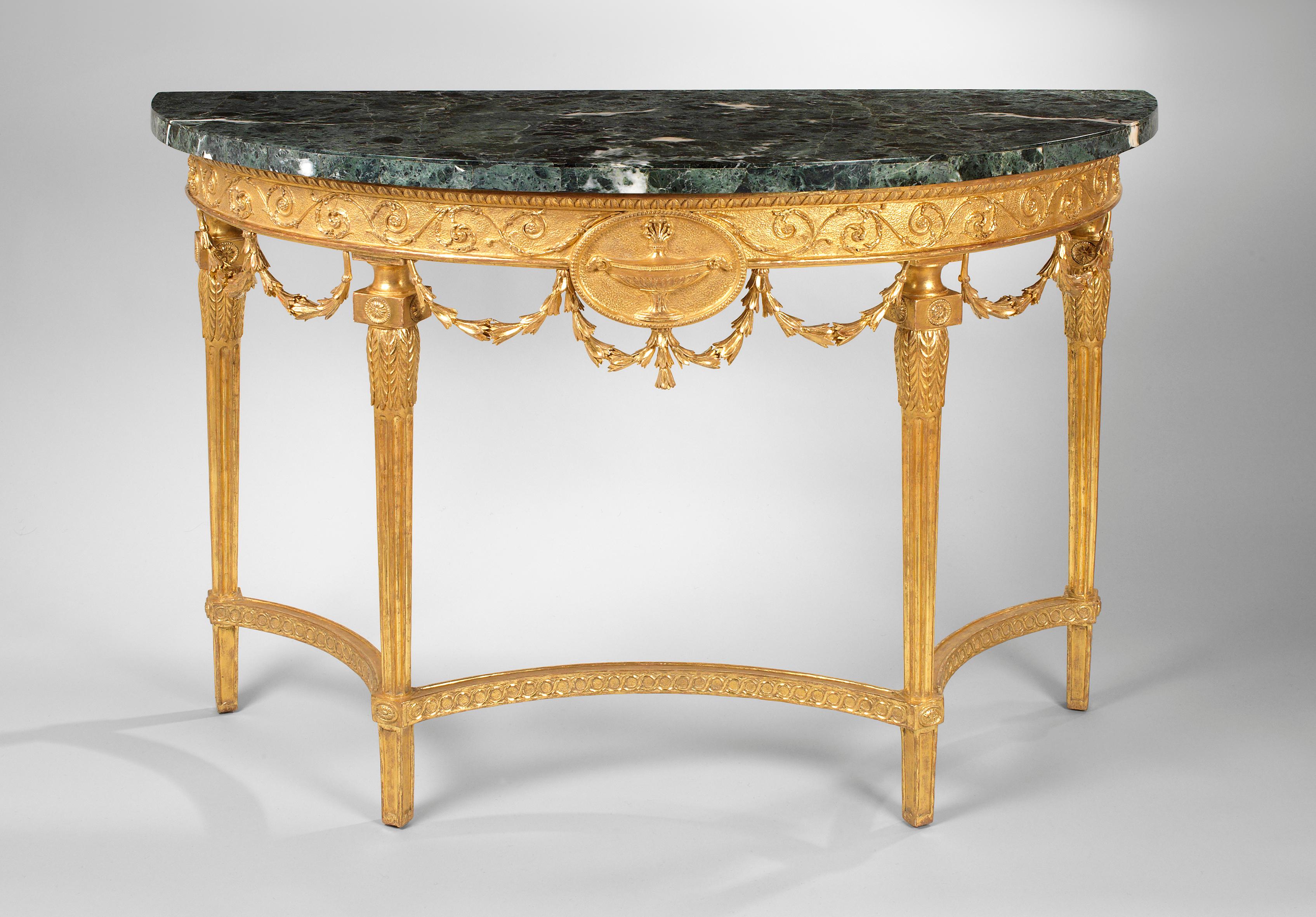 A fine pair of 18th century Adam Period carved giltwood demilune tables with marble tops above a burnished frieze with scrolling leaf; centred by a classical oval burnished medallion, decorated with a large central urn, the whole frieze being