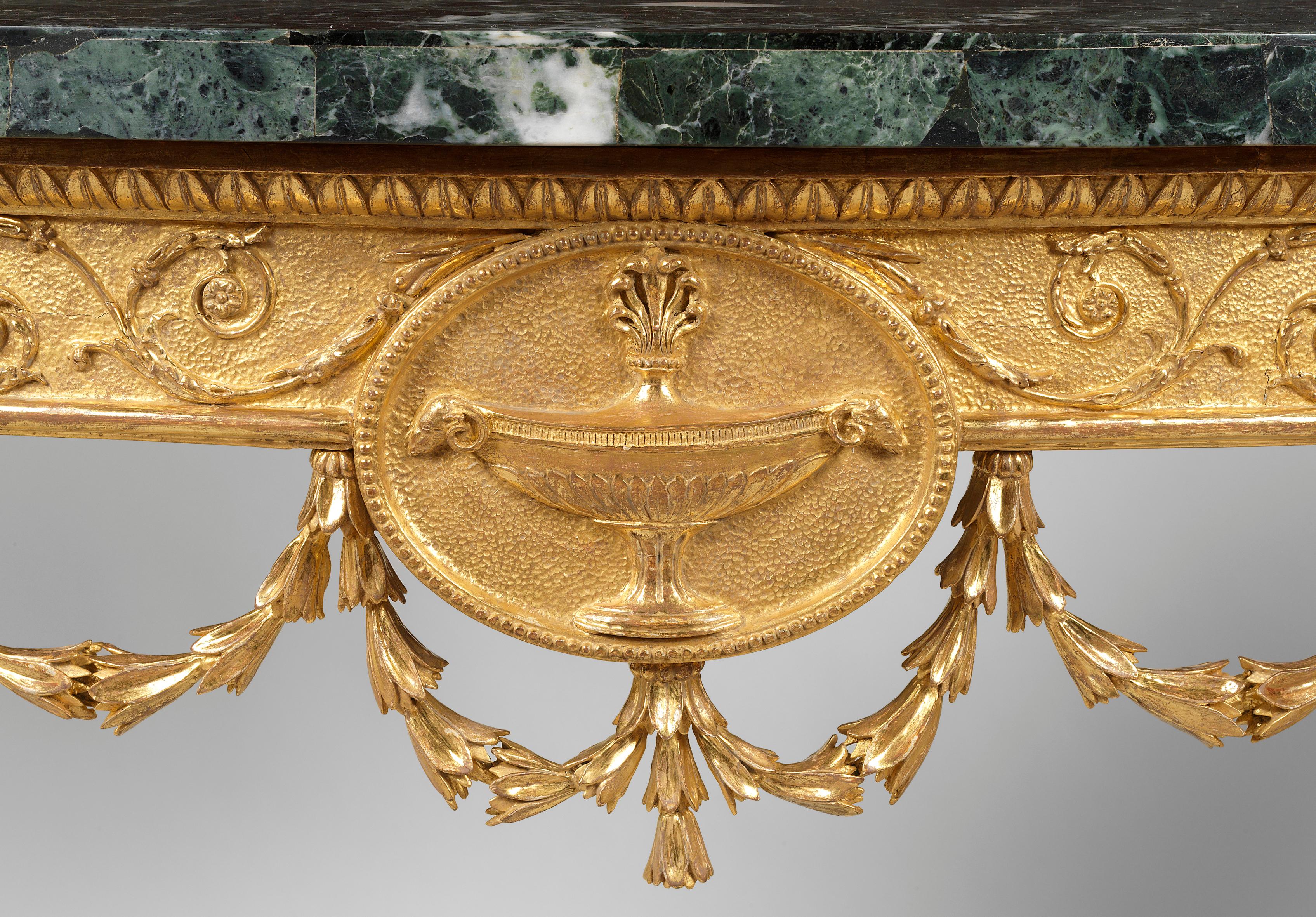 A fine pair of 18th century Adam Period carved giltwood demilune tables with marble tops above a burnished frieze with scrolling leaf; centred by a classical oval burnished medallion, decorated with a large central urn, the whole frieze being