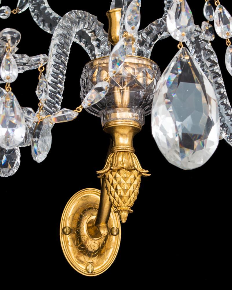 A Fine pair of ormolu-mounted and cut glass two light wall lights the oval back plates surmounted with a notched cut container, the wall lights centred by a triangularly spire this surmounted by a drop hung canopy and a Classic urn shaped finial.