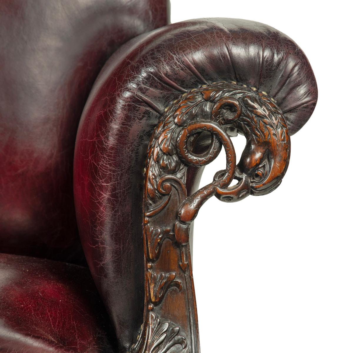A fine pair of large late Victorian mahogany eagle sofas, each with a rectangular back and scrolling armrests, the face of each arm boldly carved with an openwork eagle holding a writhing snake in its beak, above graduated flowerheads, the chair