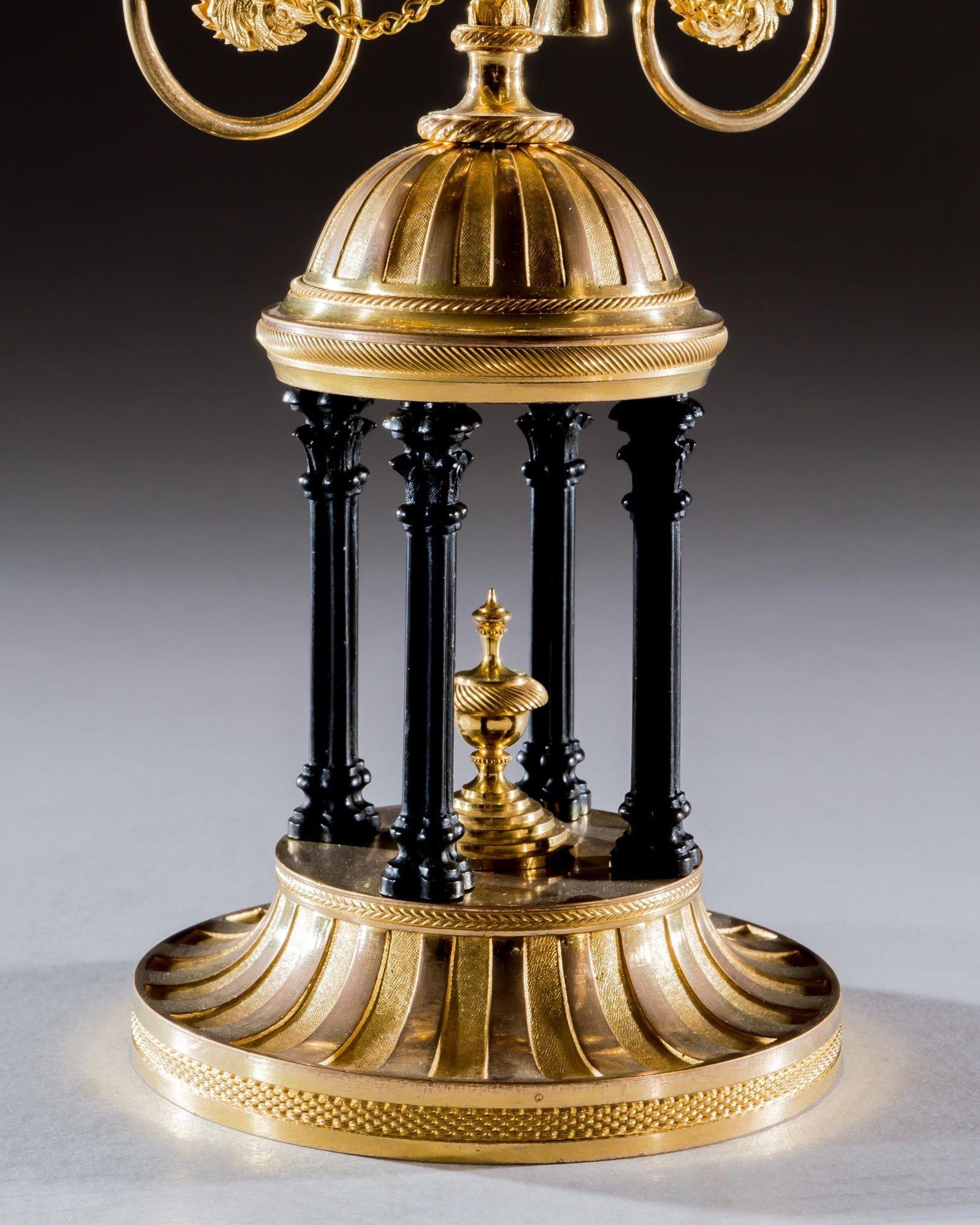 La base scanalata in ormolu con fini motivi zigrinati e l'urna centrale montata con colonne in bronzo. La cupola è dotata di tre bracci a volute foliate, due dei quali sostengono le vaschette di raccolta e i beccucci delle candele, mentre il terzo è
