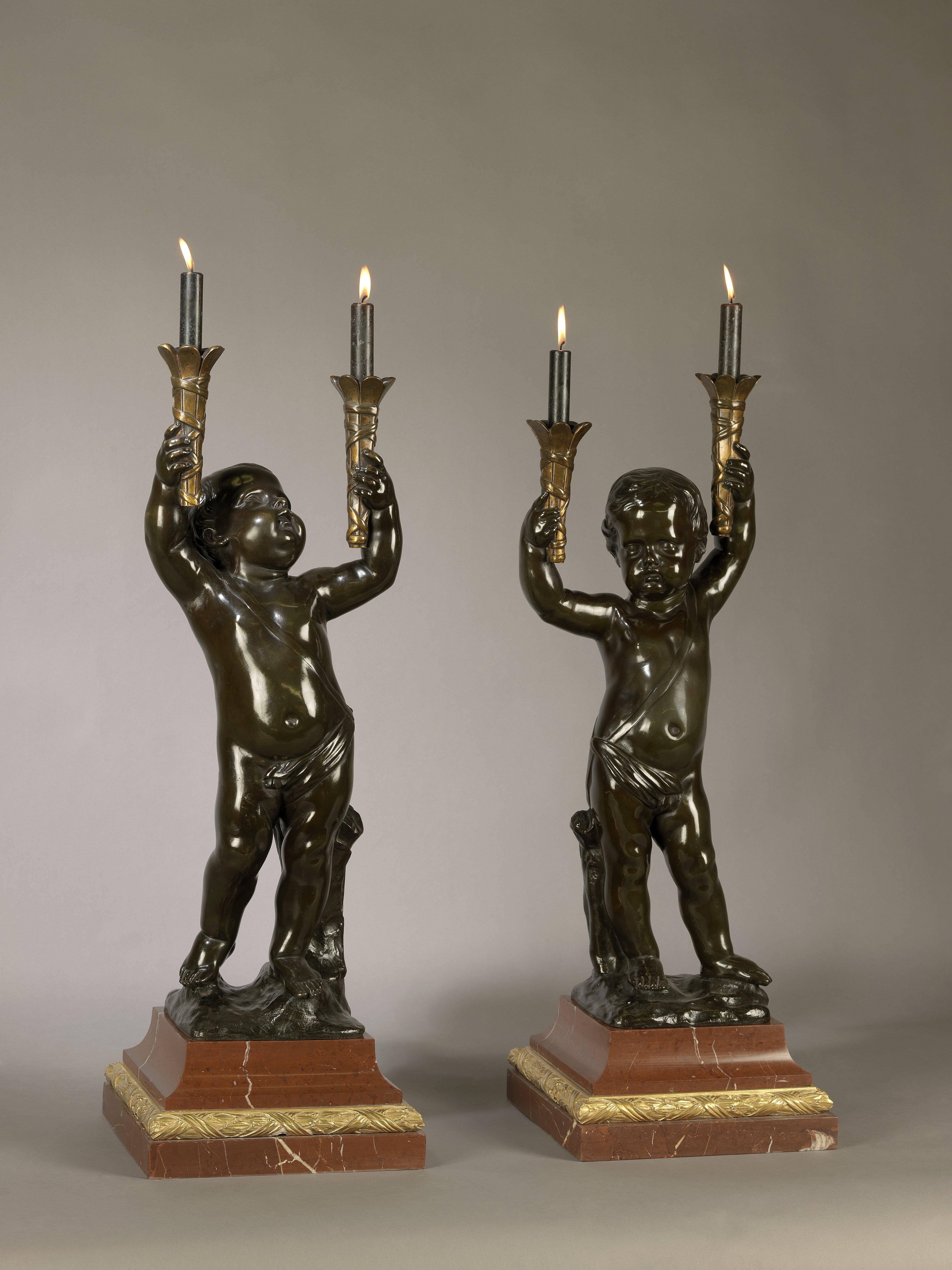 A fine pair of patinated bronze figural torchères.

French, circa 1890.

Each torchere is finely modelled and cast in the form of an expressive putti figure holding aloft a pair of ribbon tied torches. The figures stand on naturalistic rocky