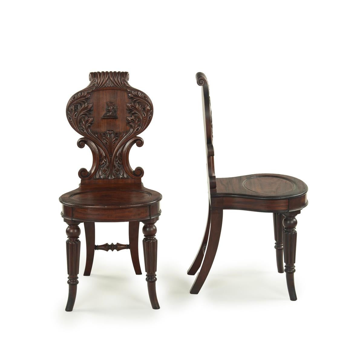 A fine pair of Regency mahogany armorial hall chairs attributed Gillows, each with an ogee back supported on C-scrolls and circular dished seat raised on turned and reeded outswept front legs, the rectangular section back legs joined by a shaped