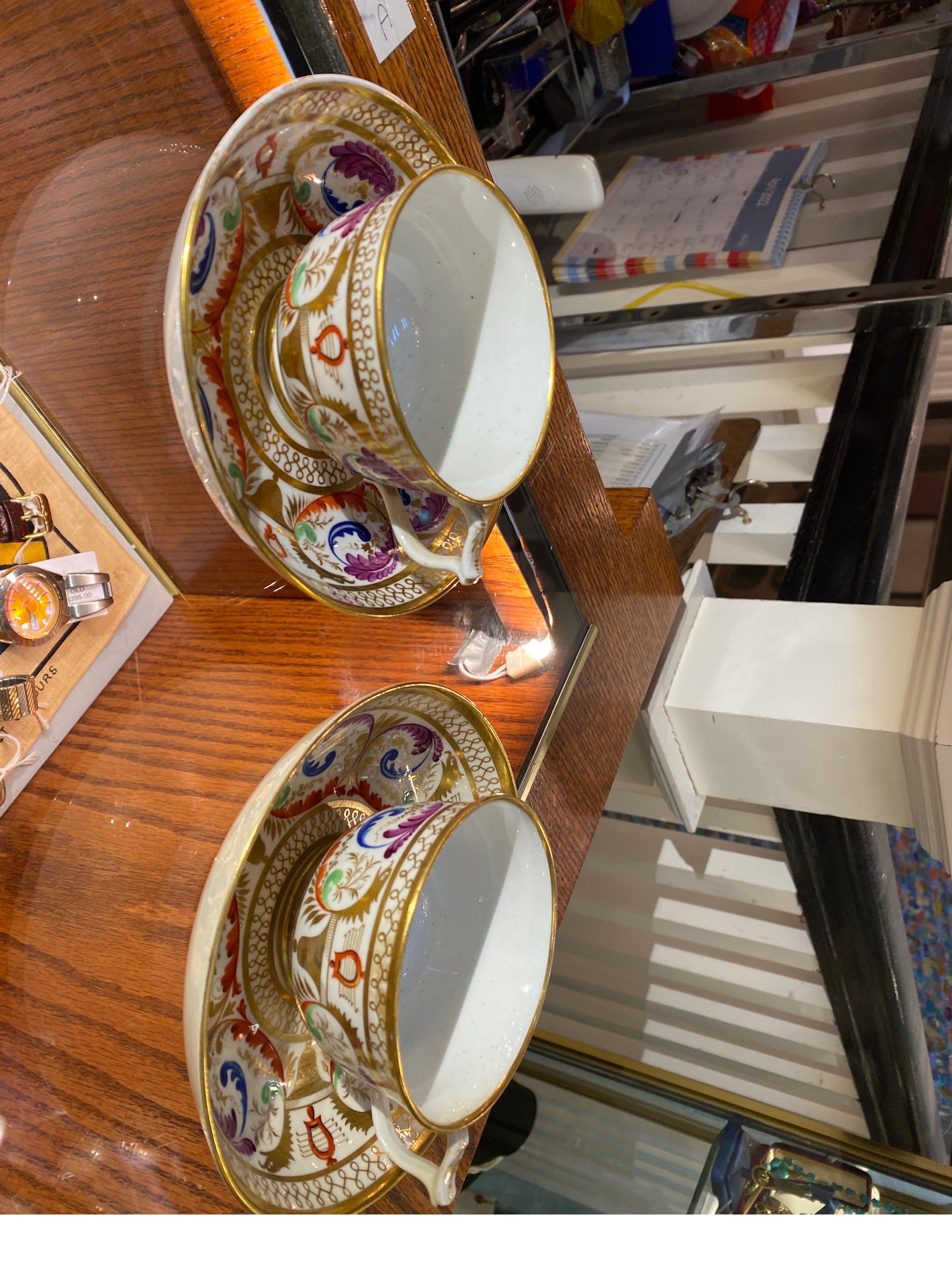 A stunning pair of hand painted porcelain English Regency tea cups and saucers. The vibrantly colored decoration with gilt accents. The red underglaze mark was used from 1806 to 1823.