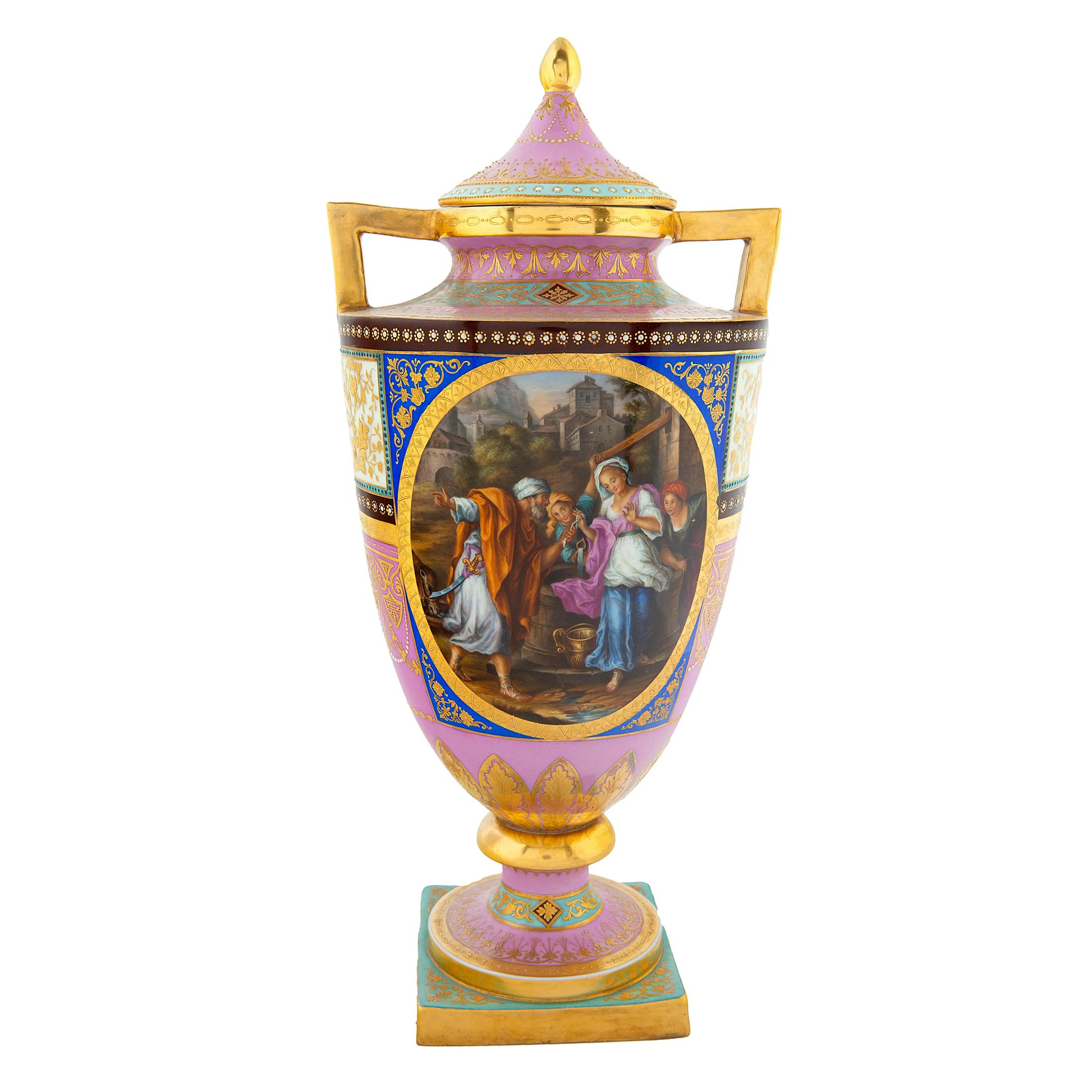 The pair of Austrian ovoid-form porcelain vases and cover with sharply angular gilt handles, Ackermann & Fritze, Rudolstadt-Volkestedt. The bright pink body centered on either side with a pair of narrative scenes against a cobalt ground, with pale