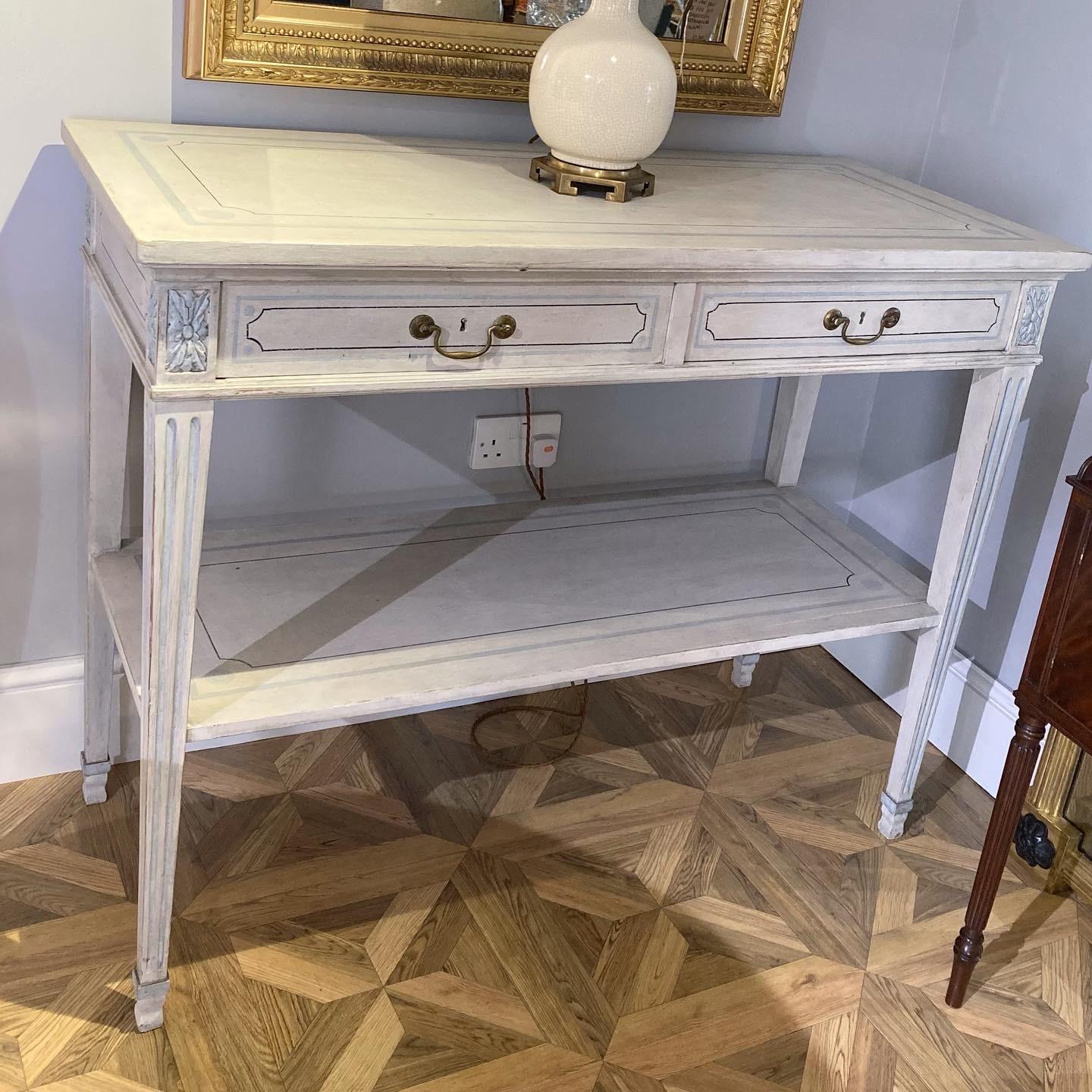 A good sized pair of white painted 19th century continental console/side tables. Each table sits on fluted tapered legs terminating on spade feet with carved floral rosettes to the top.

They each feature 2 brass-handled drawers with a lower-height