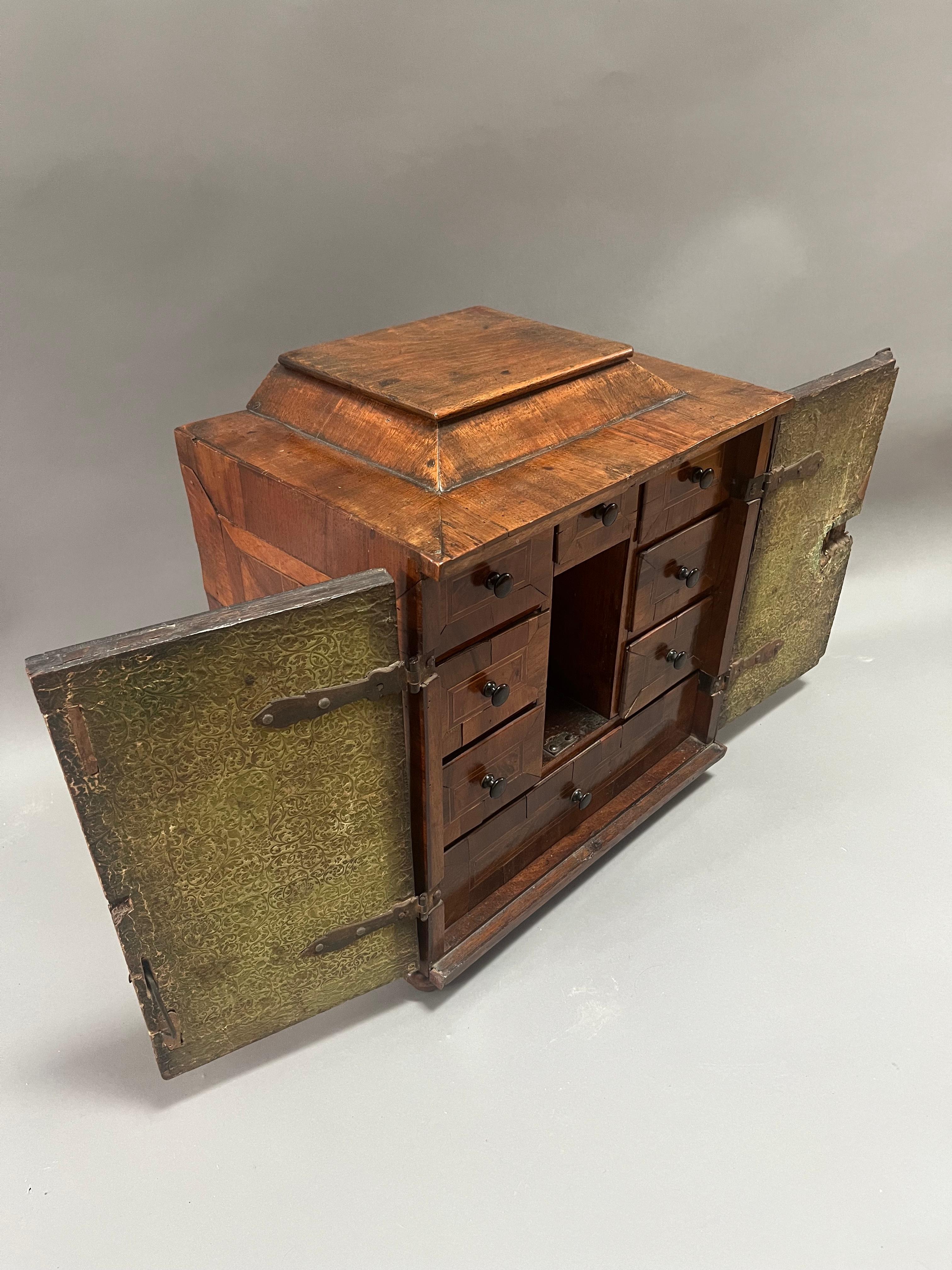 Made Of richly patinated Walnut with a lustrous deep color. Intricate Parquetry decorated sides and two doors. Original strap hinges conceal eight cross banded drawers and three further smaller drawers standing on four small bun feet. Southern