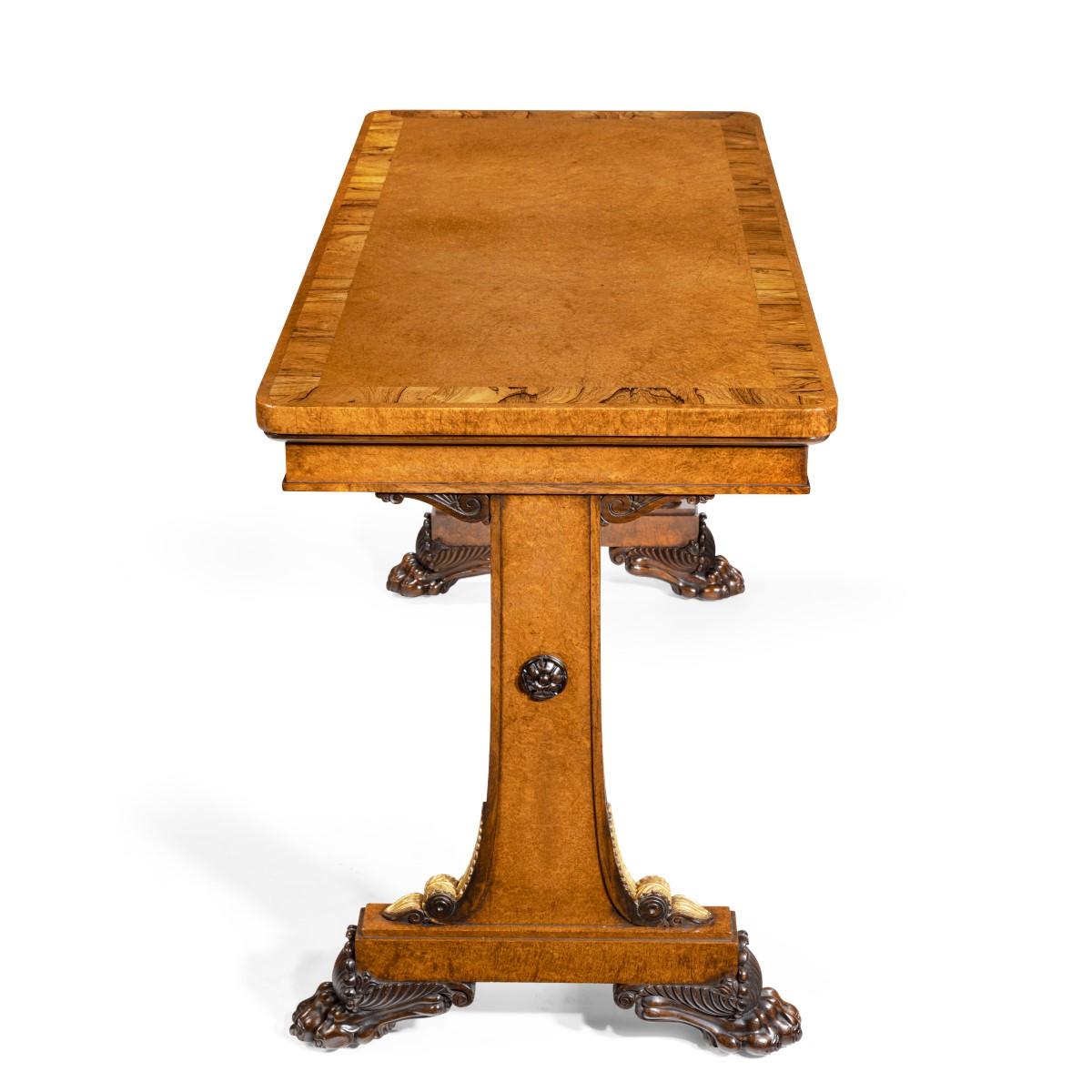 Le plateau rectangulaire en surplomb, aux angles arrondis, est presque entièrement plaqué d'amboyna avec un large bandeau transversal en palissandre. Sous le plateau se trouve une frise étroite, et la table repose sur deux supports d'extrémité