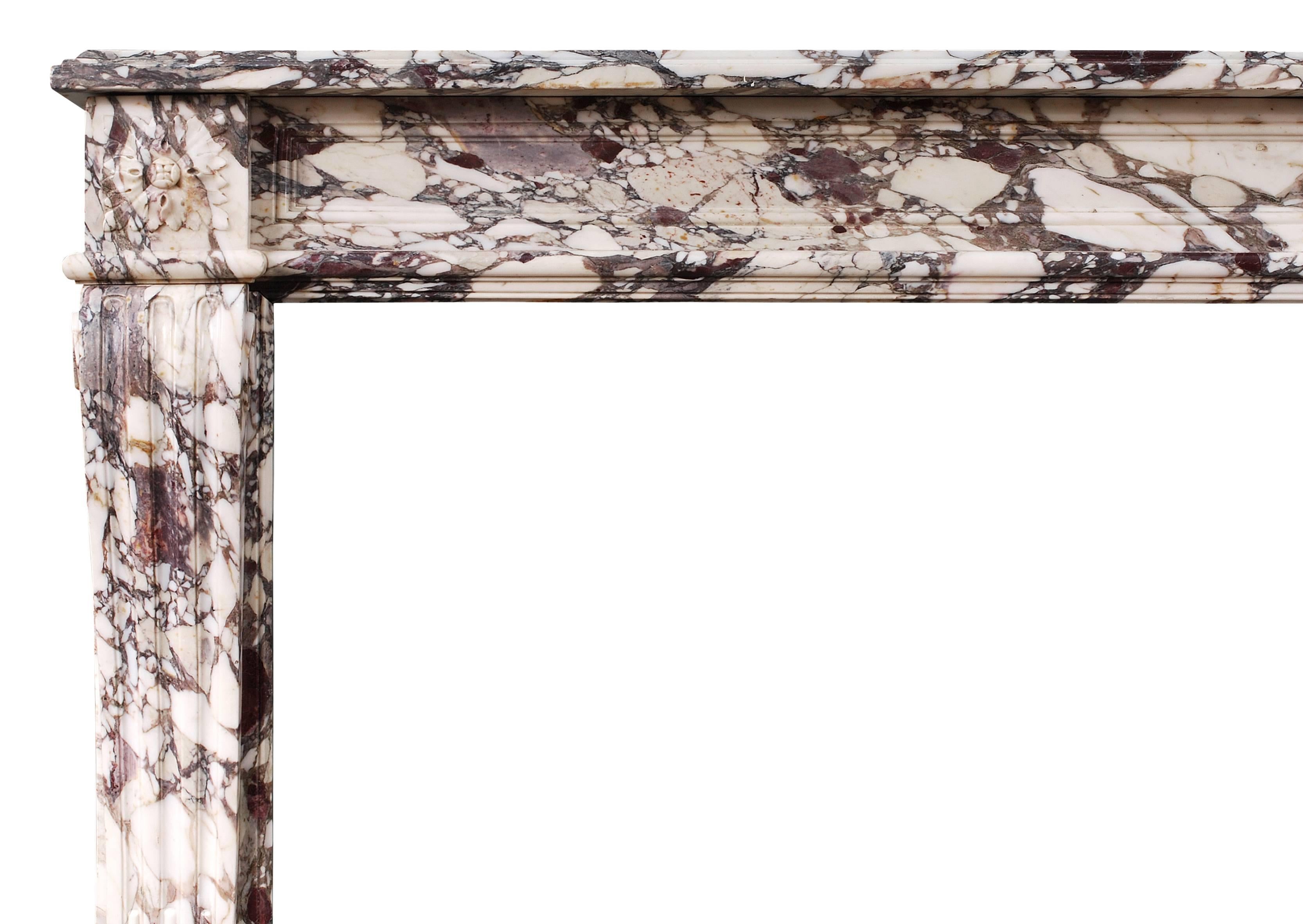 Cheminée française de style Louis XVI du milieu du XIXe siècle en marbre Brèche Violette. Les montants profilés et cannelés sont surmontés de patères carrées sculptées, d'une frise de panneaux et d'une tablette moulurée, vers 1840. Marbre très