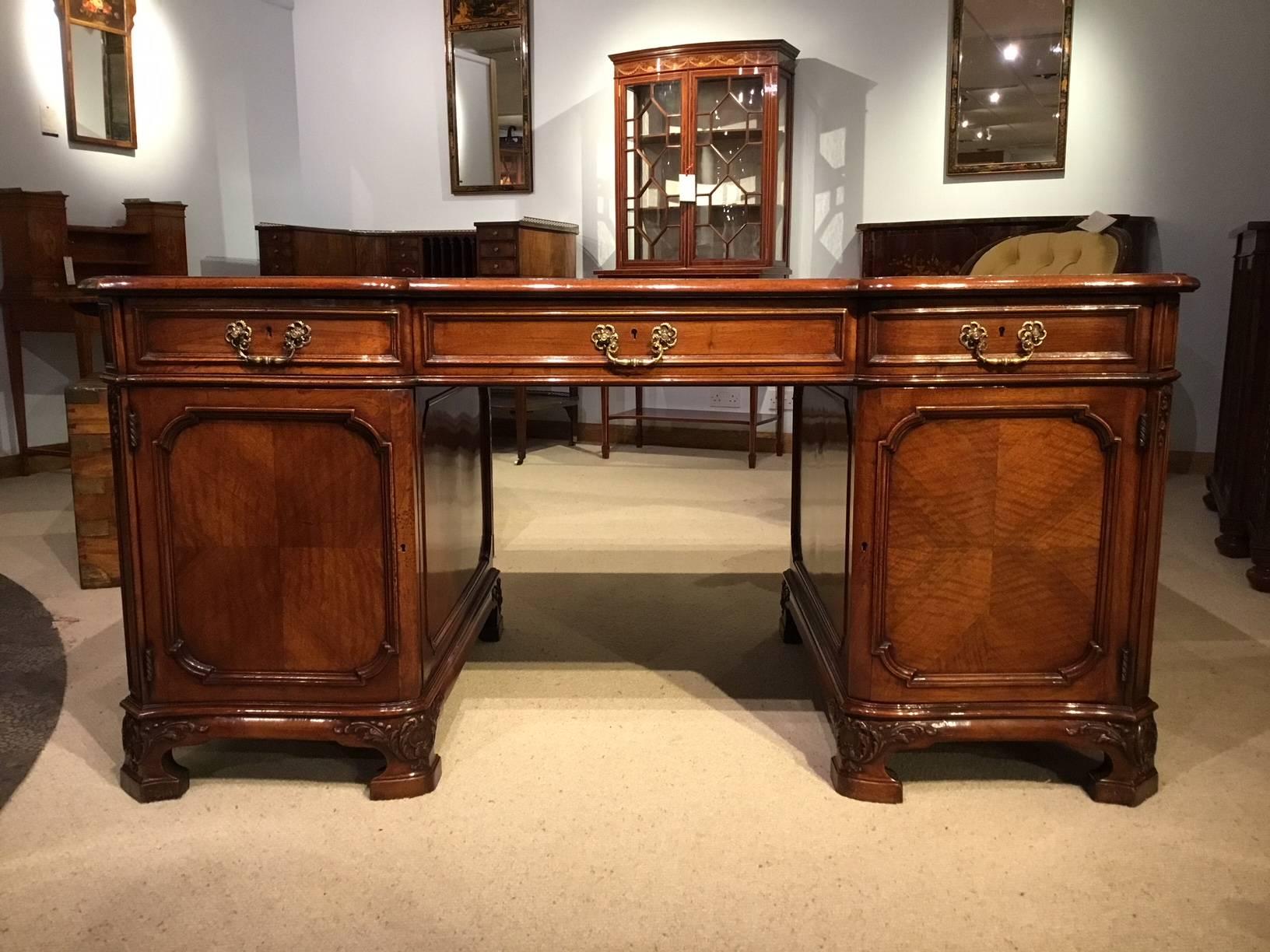 A fine quality figured walnut Edwardian Period pedestal desk. Having a solid walnut top of serpentine outline with a red gilt and blind tooled leather writing insert, above the three rectangular walnut lined drawers with Chippendale style pierced