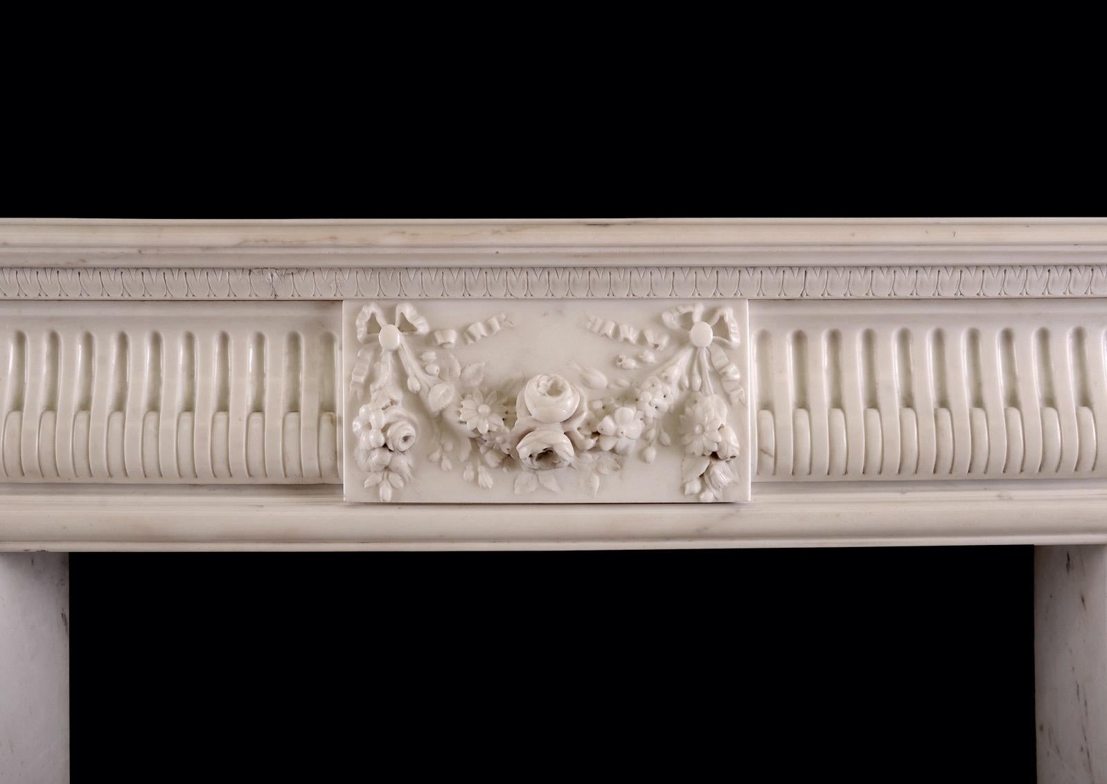 A delicate French Louis XVI style fireplace in white Statuary marble. The stop-fluted jambs surmounted by square carved paterae. The shaped frieze with centre block featuring finely carved swags of flowers and foliage. The shaped, moulded shelf with