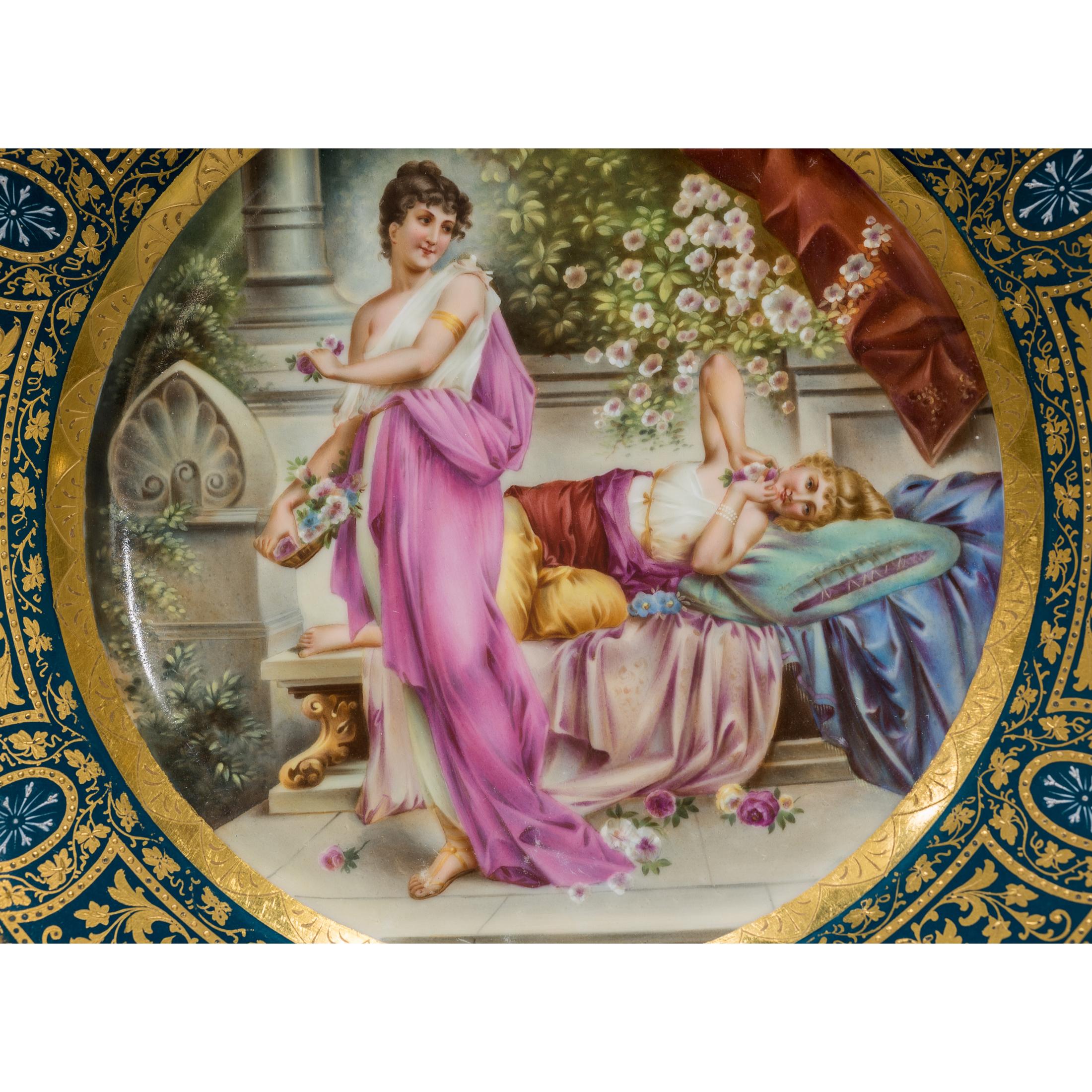 Exquisite Royal Vienna portrait porcelain gilded cabinet plate featuring hand-painted illustrations of two beautiful young neoclassical women lounging in a garden. The cobalt blue border is finished with gold trim of grape vines, with leaflike