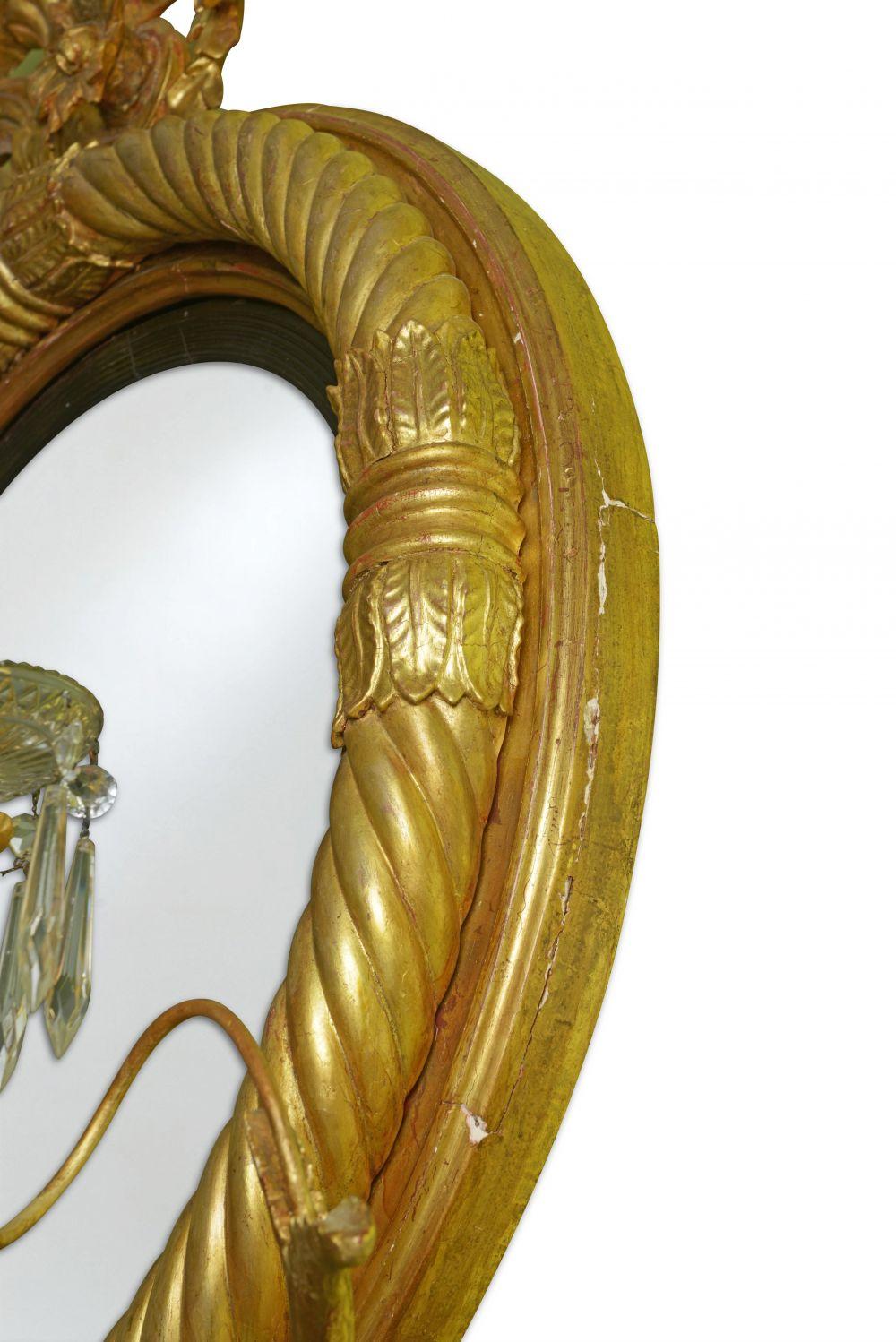 The convex mirror plate within an ebonies reeded surround and spiral reeded frame with lotus-leaf clasps; surmounted by a pair of addorsed dolphins on a rockwork plinth flanked by scrolling foliage; Issuing four outscrolled candlearms with glass