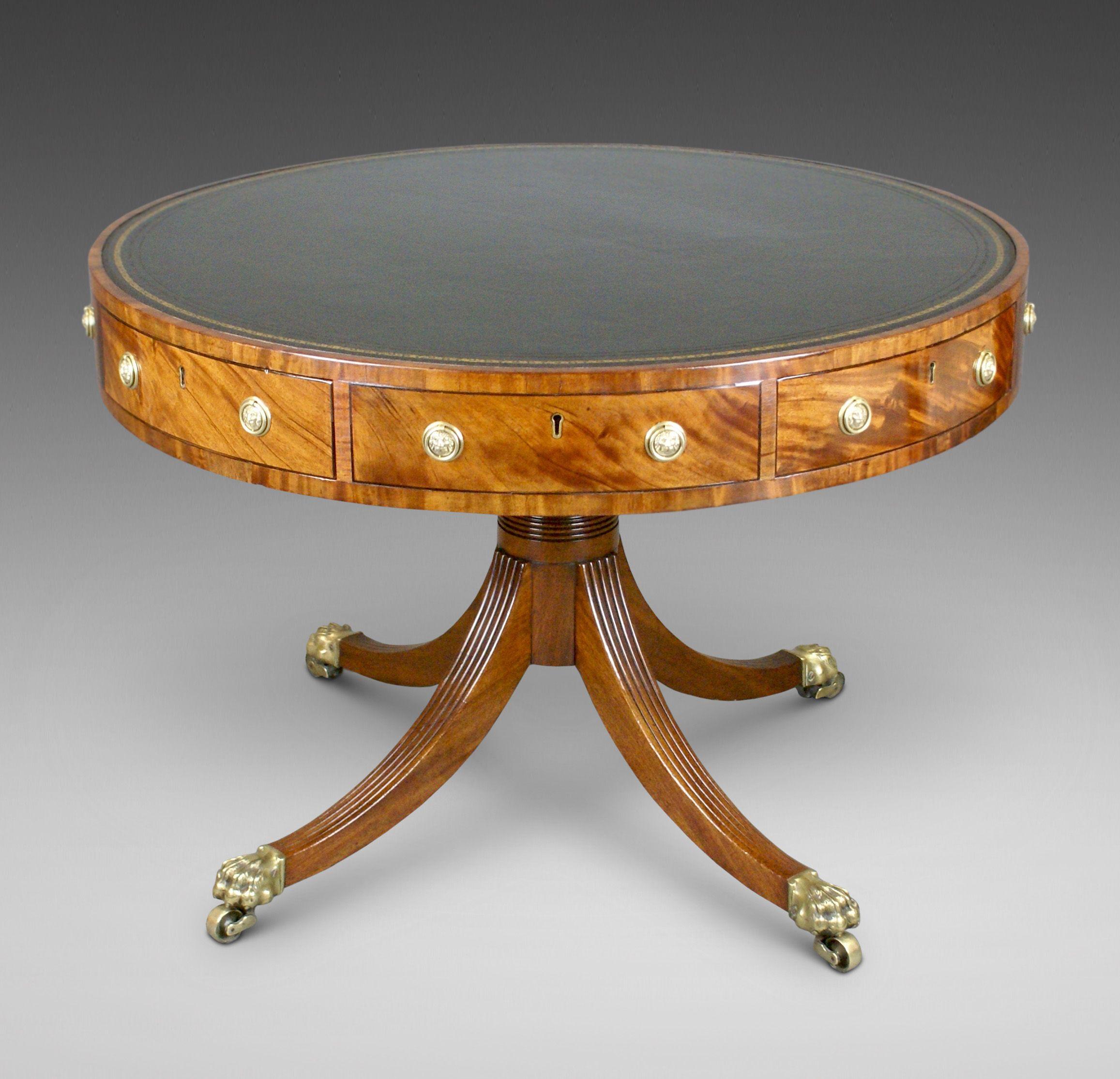 A Fine Regency Period Mahogany Drum table. Raised on four reeded swept legs with original brass paw castors and with a turned gun -barrel column. The top with four frieze drawers and four dummies all with lions mask ring handles (replacements). The