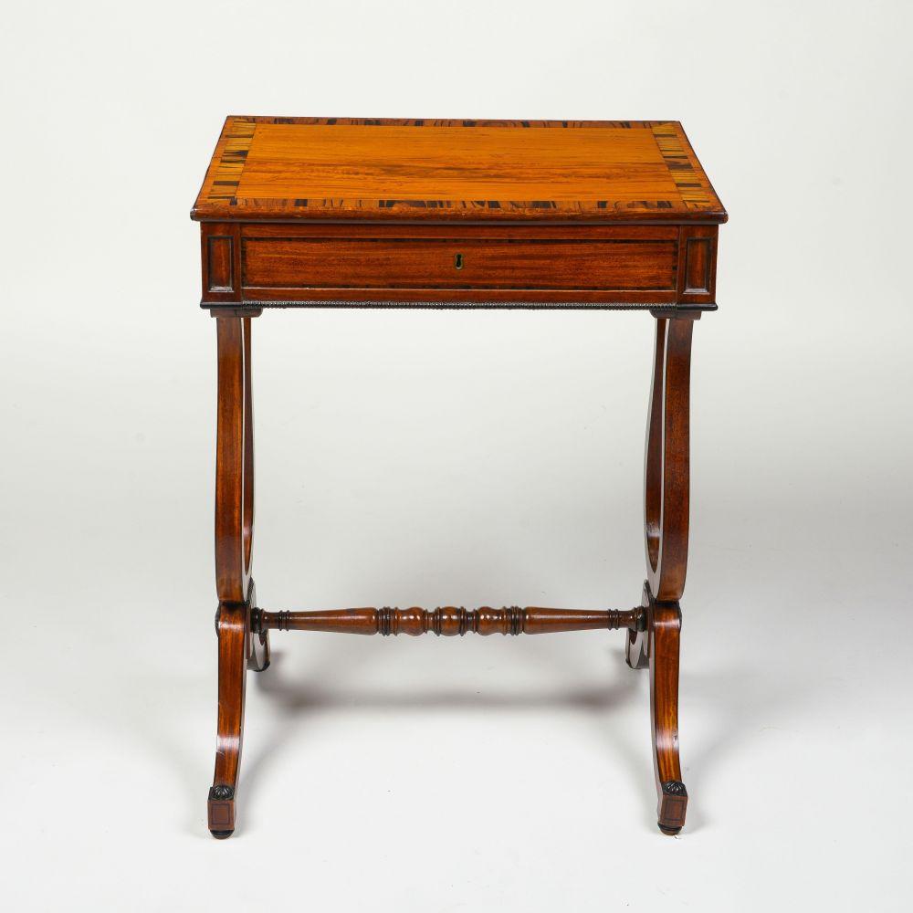 The rectangular overhanging top with broad calamander banding, over one frieze drawer fitted with chased brass knobs, set between recessed retangular panels above an ebonized beaded edge; raised on lyre-from end supports on downswept legs and joined