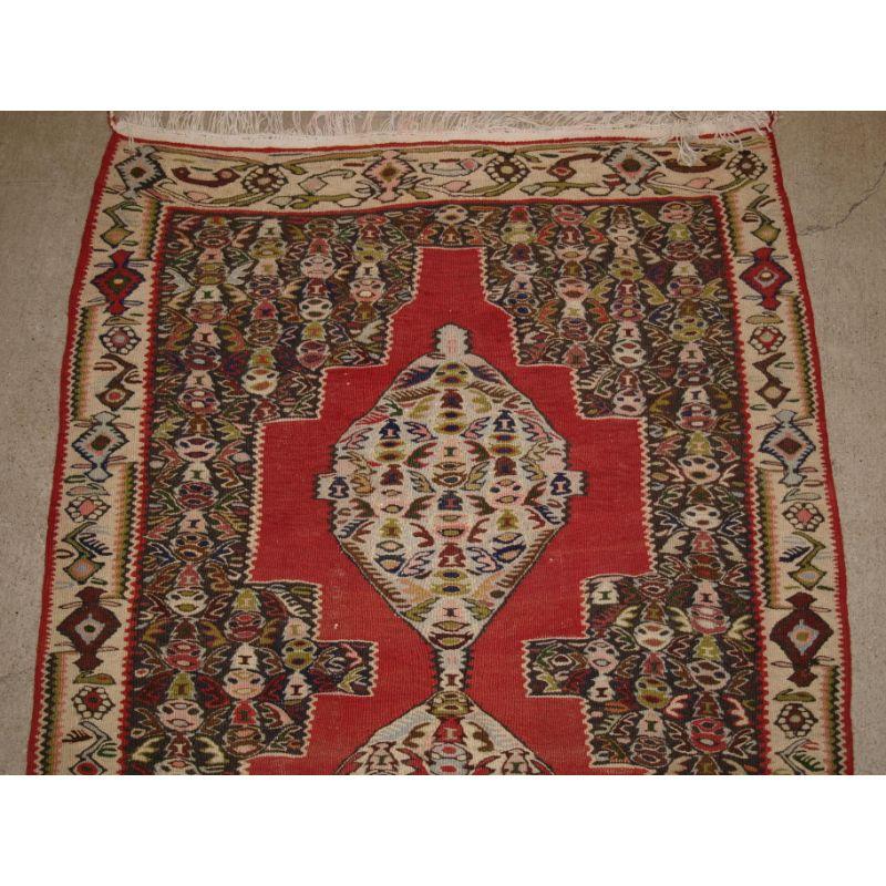 A fine Senneh kilim runner with soft colours and a linked medallion design.

Senneh kilim runners of this size are scarce in the market today, this example has a very traditional Senneh floral design, the soft red ground is complimented by the ivory